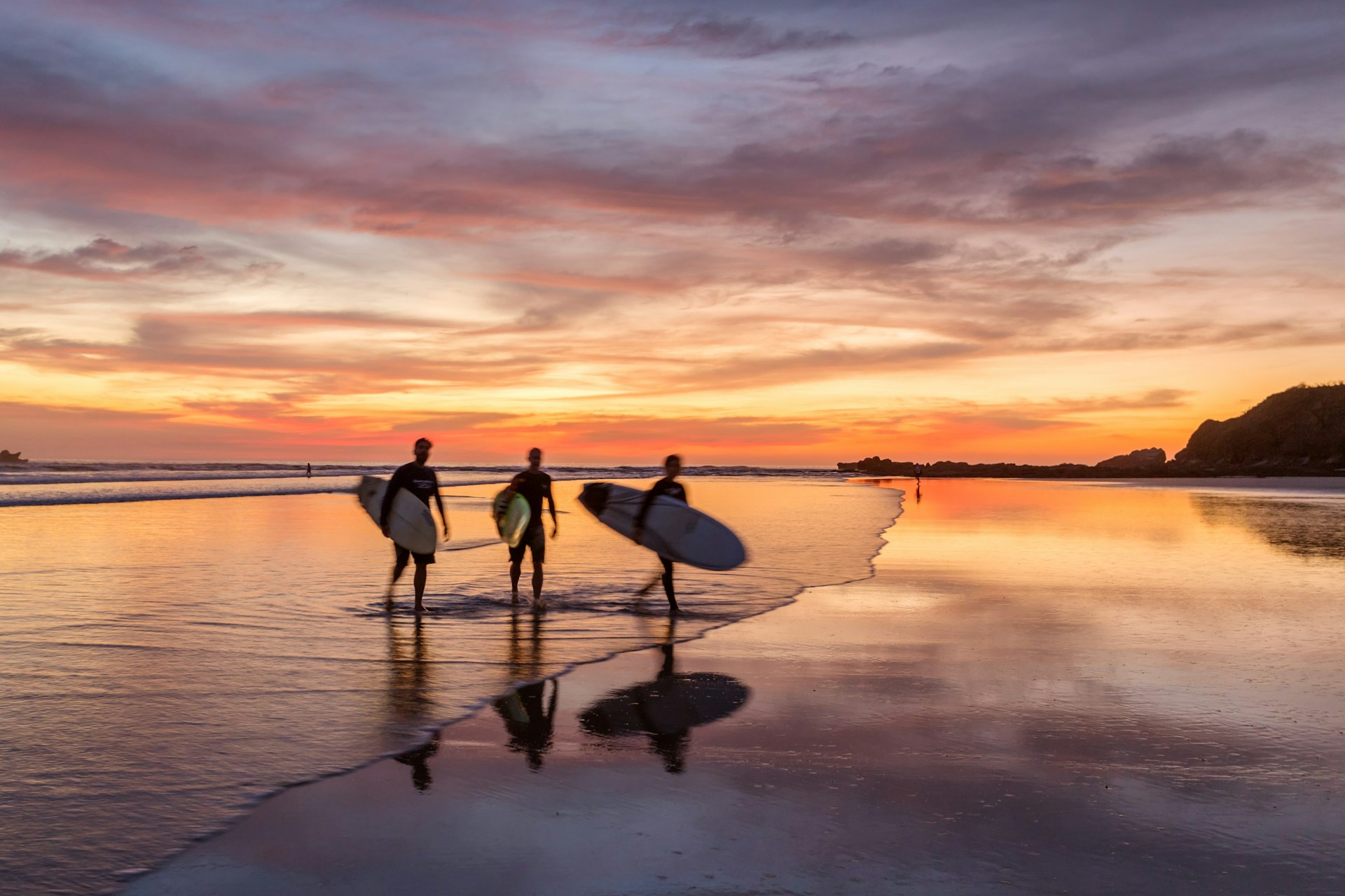 Surfers at sunset walking on beach, Costa Rica. 