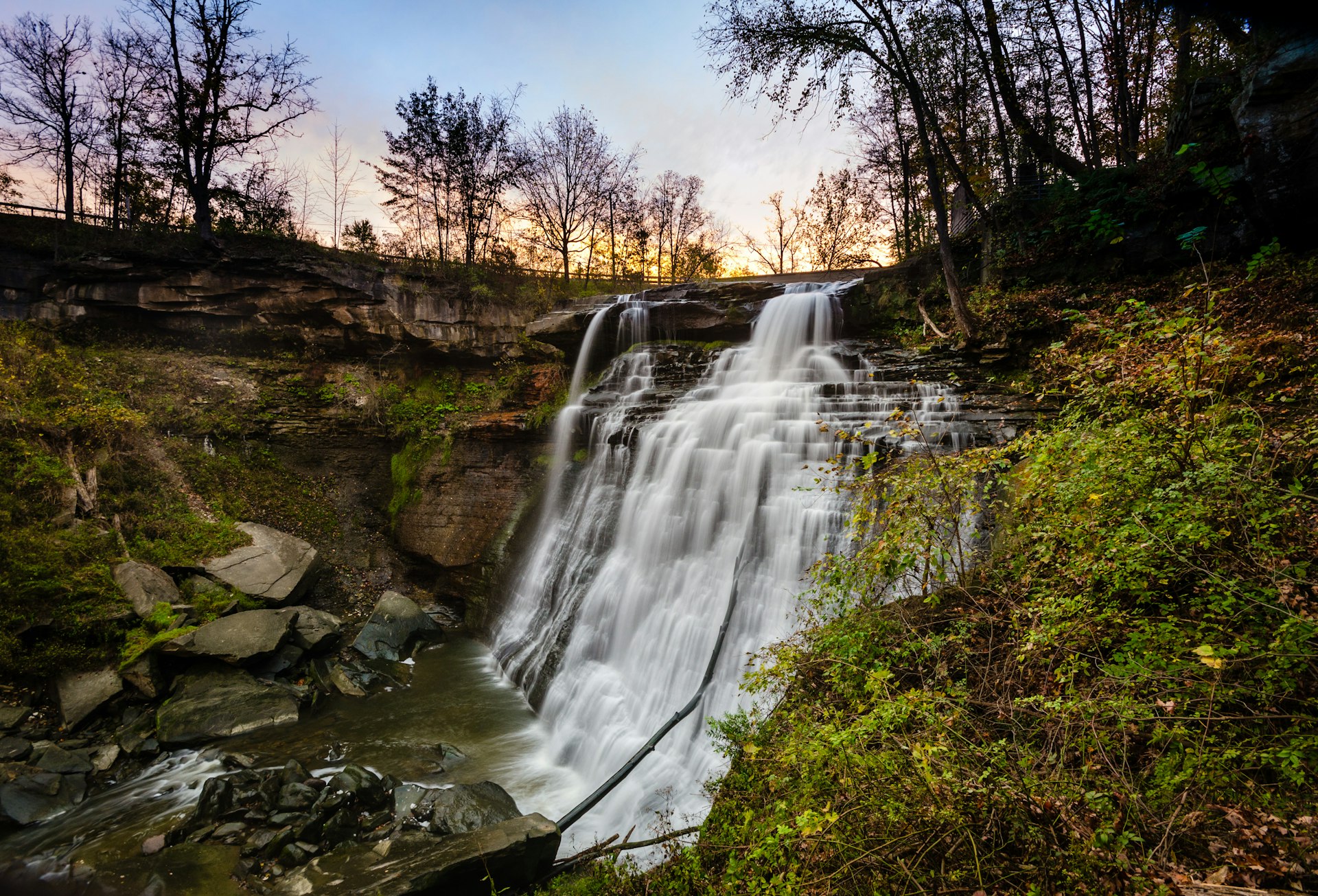 A wide waterfall with several tiers at the top, plunging onto a rocky ledge