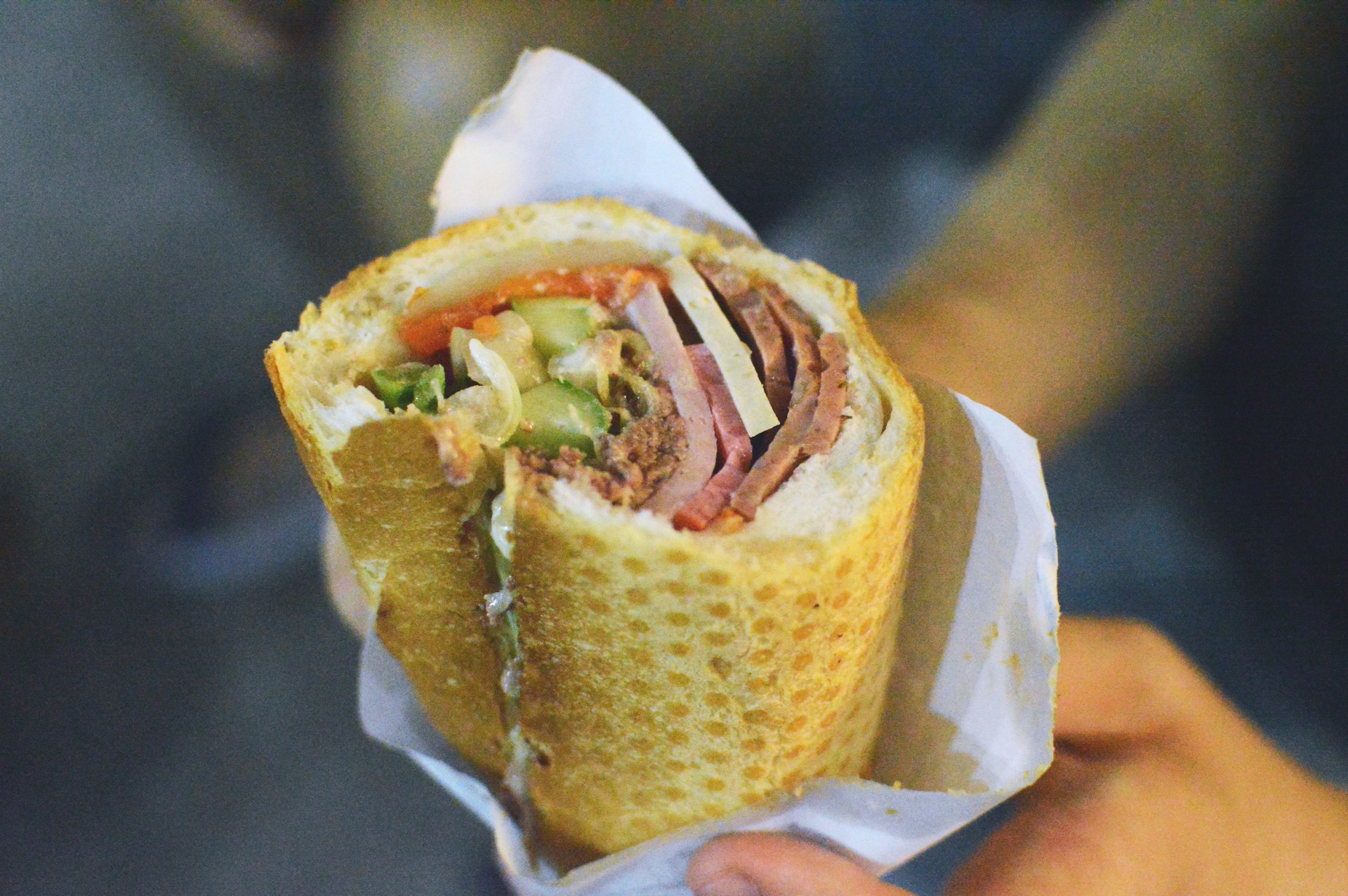 A close-up shot of someone holding a bánh mì roll in Ho Chi Minh City. The roll consists of a small section of baguette, that is stuffed with fillings.