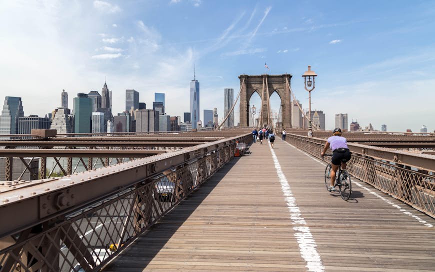 Bakifrån Av Kvinnan Cyklar På Brooklyn Bridge I Staden Mot Himlen