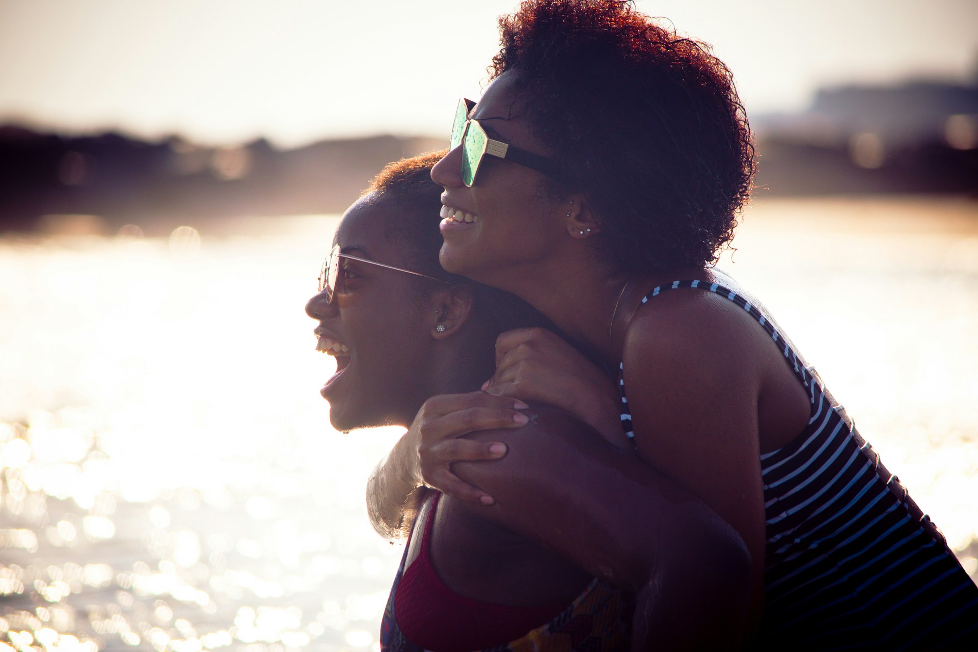 Two black women hug and smile at the beach together.