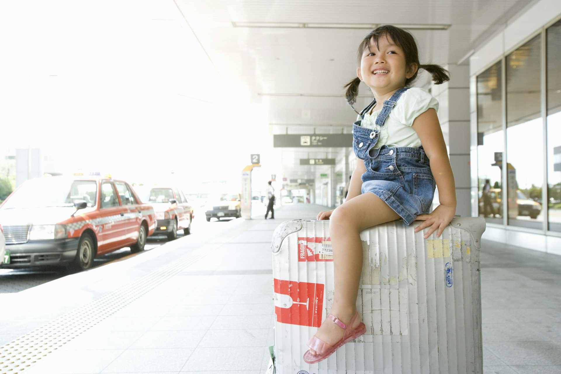 A girl sits on a suitcase outside an airport in Japan 