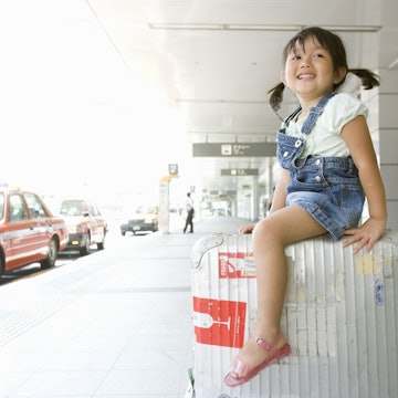 A girl rides suitcase by cabstand in airport