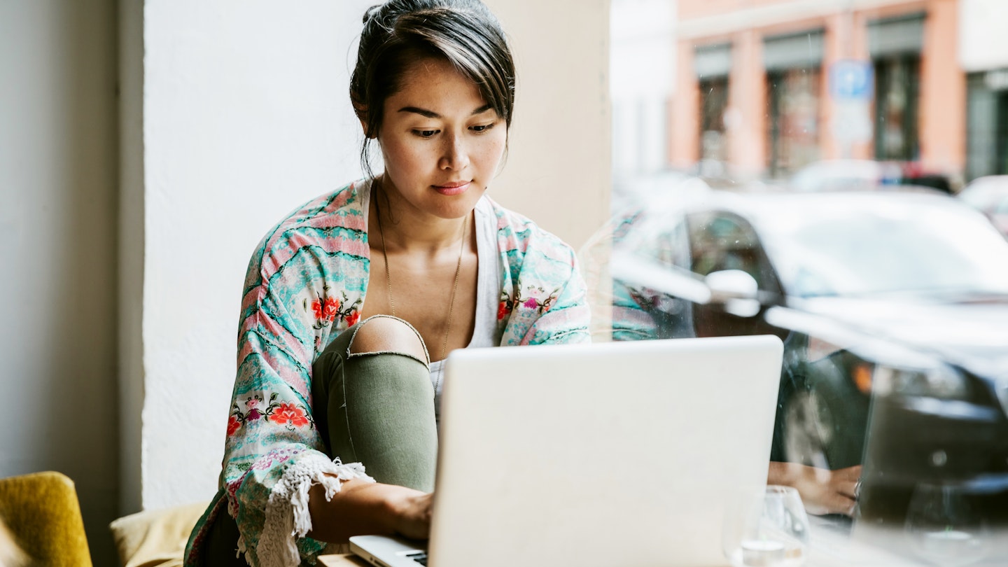 Young woman sitting at the window of a Berlin cafe and working from her laptop.