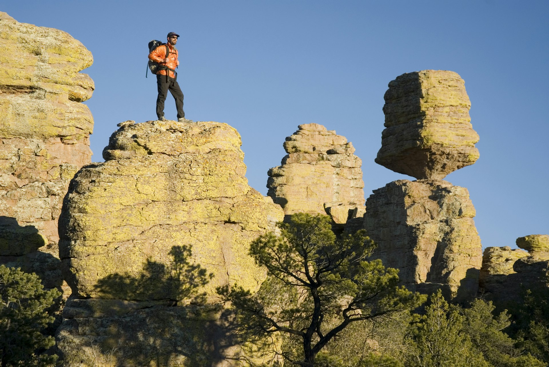 Man stands on rock near Balanced Rock; a large boulder teetering on a narrow plinth