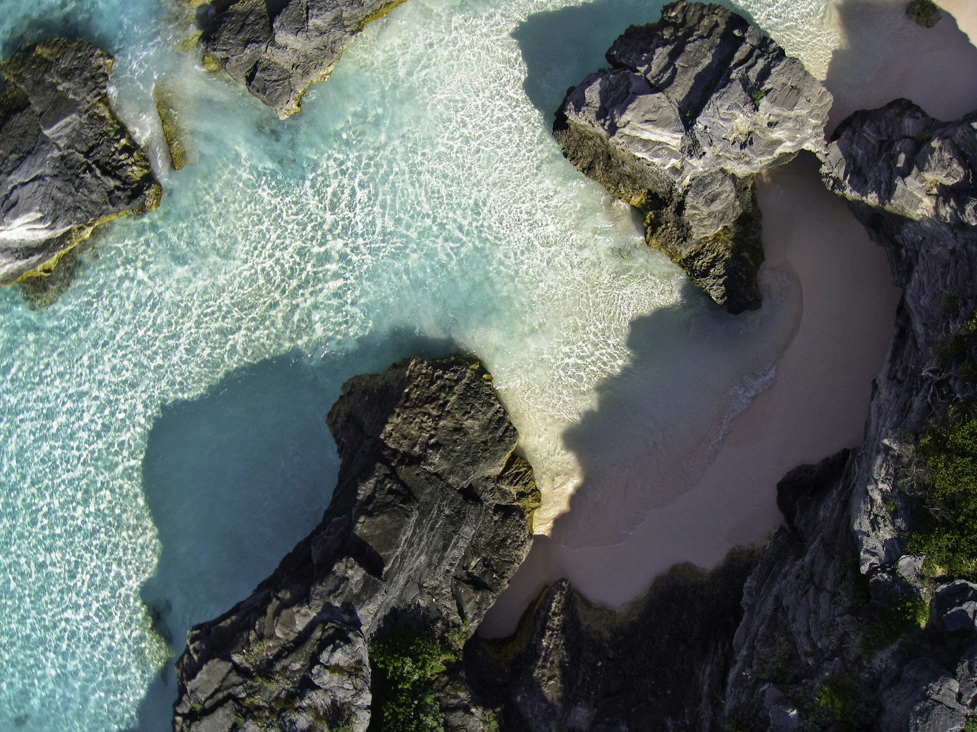An aerial view of rock formations with pockets of pink coral sand on the beach past the end of Bermuda's Horseshoe Bay