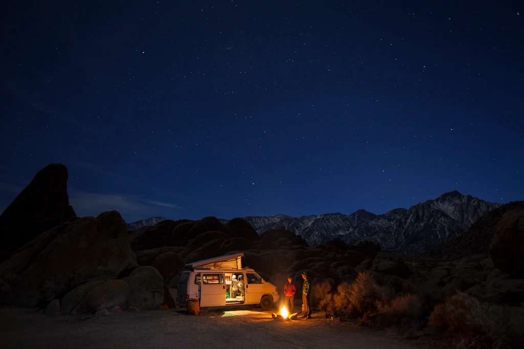 Two friends standing by campfire at night while camping in Alabama Hills Recreation Area, Lone Pine, California, USA