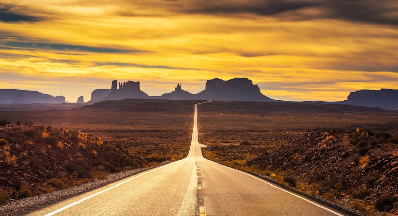 Empty desert road leading to Monument Valley, as seen from Forrest Gump Point during sunset.