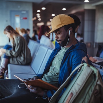 Young man and multi-ethnic crowd sitting on bench and waiting for flight departure at airport