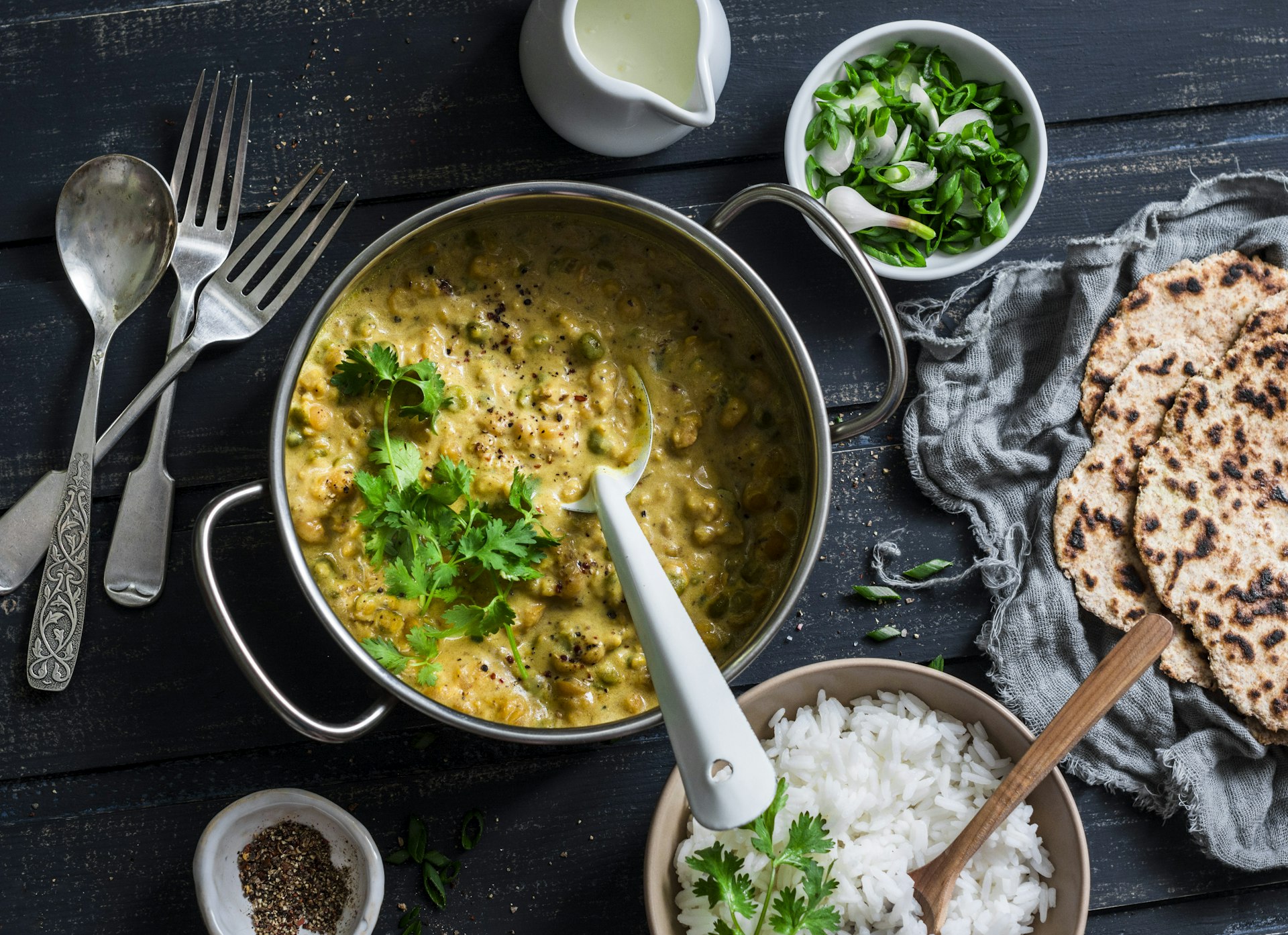 Indian dhal in cooking pan with jasmine rice, coriander and naan on dark background, top view