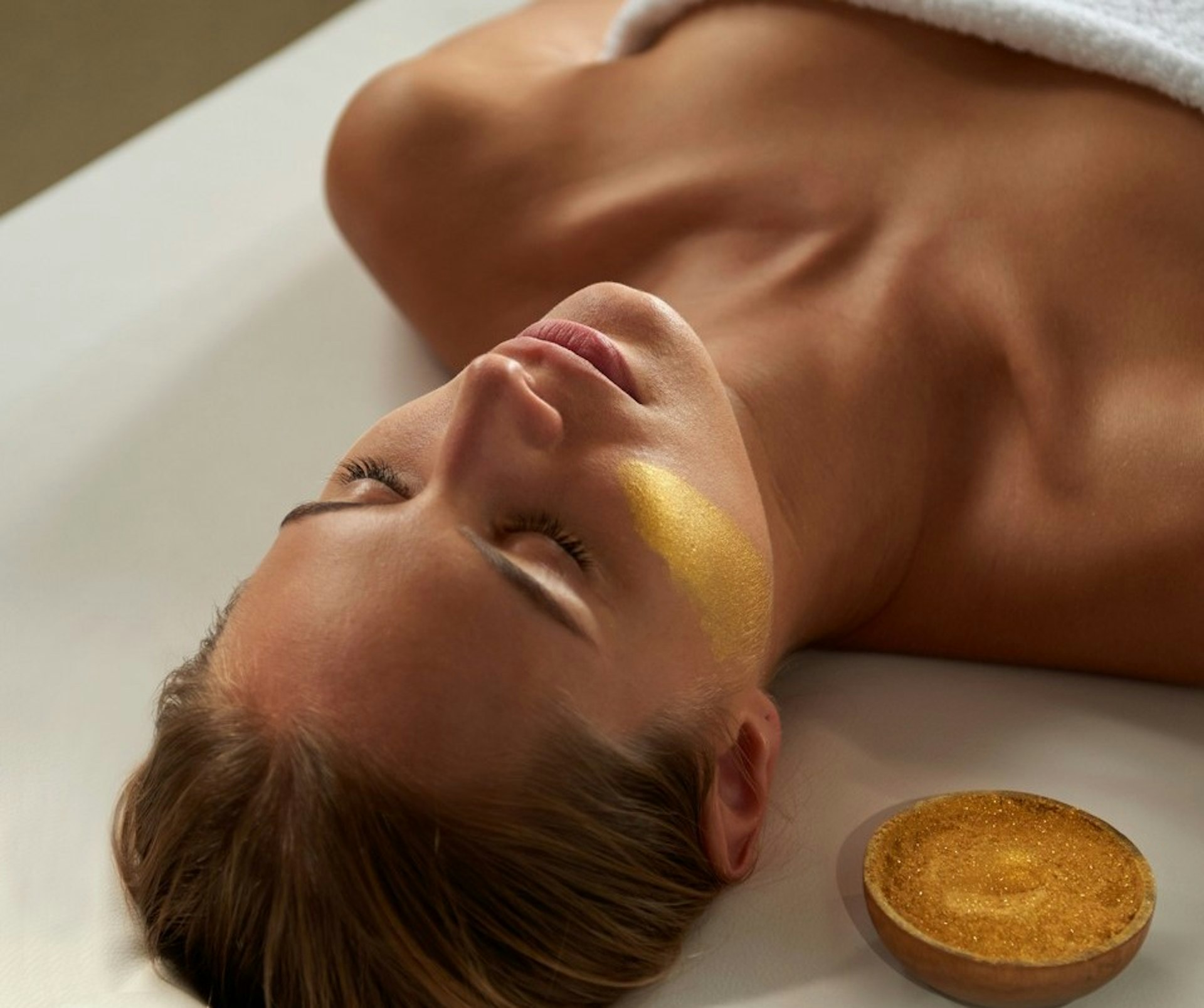 A woman enjoys a facial spa treatment with a cream that is gold in colour.