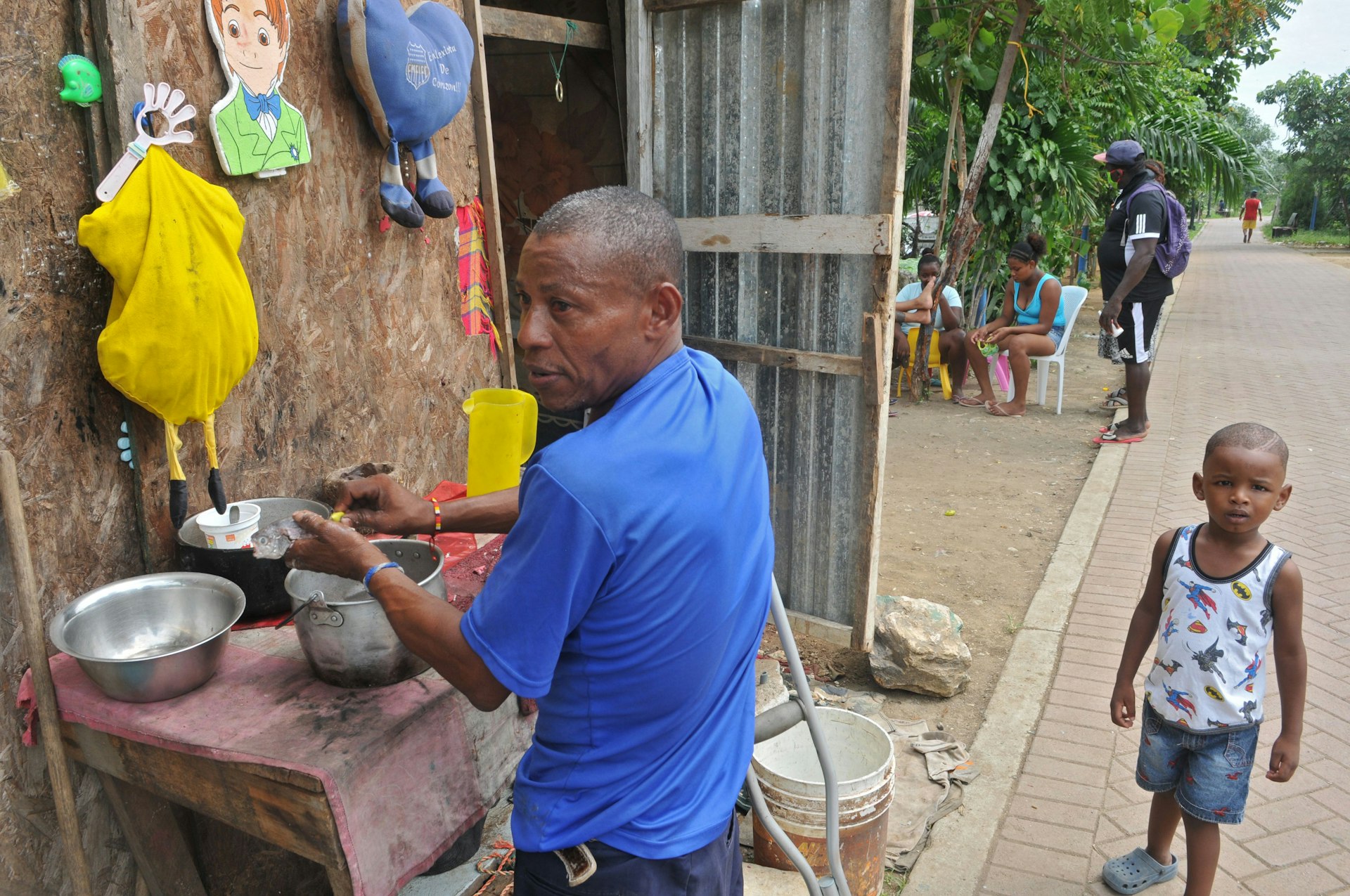 A man prepares a meal in a street of the Nigeria neighbourhood in the Isla Trinitaria section of southern Guayaquil, Ecuador. A young boy stands next to him looking at the camera.  