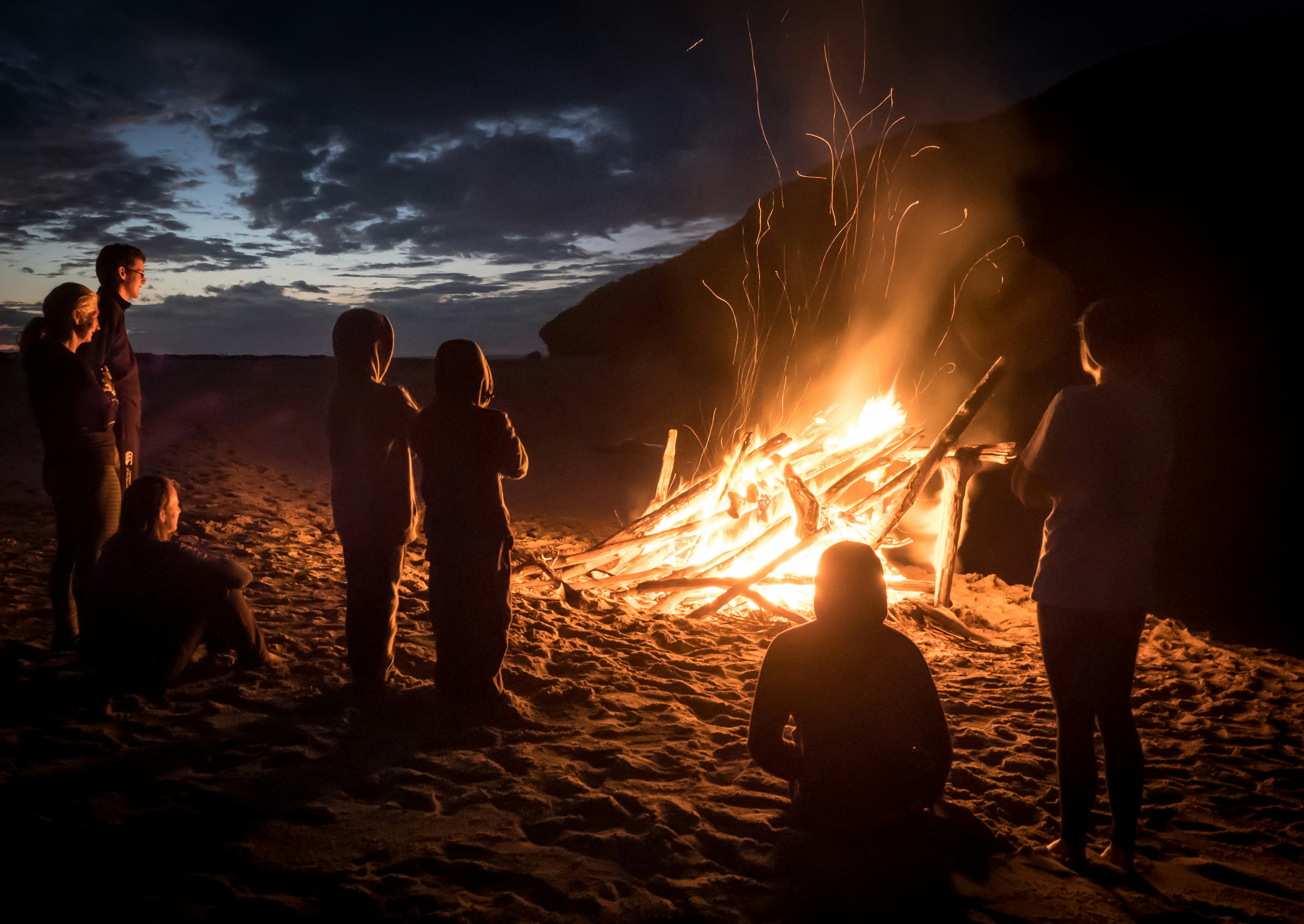 Family sit around a beach camp fire in Heaphy Track, New Zealand