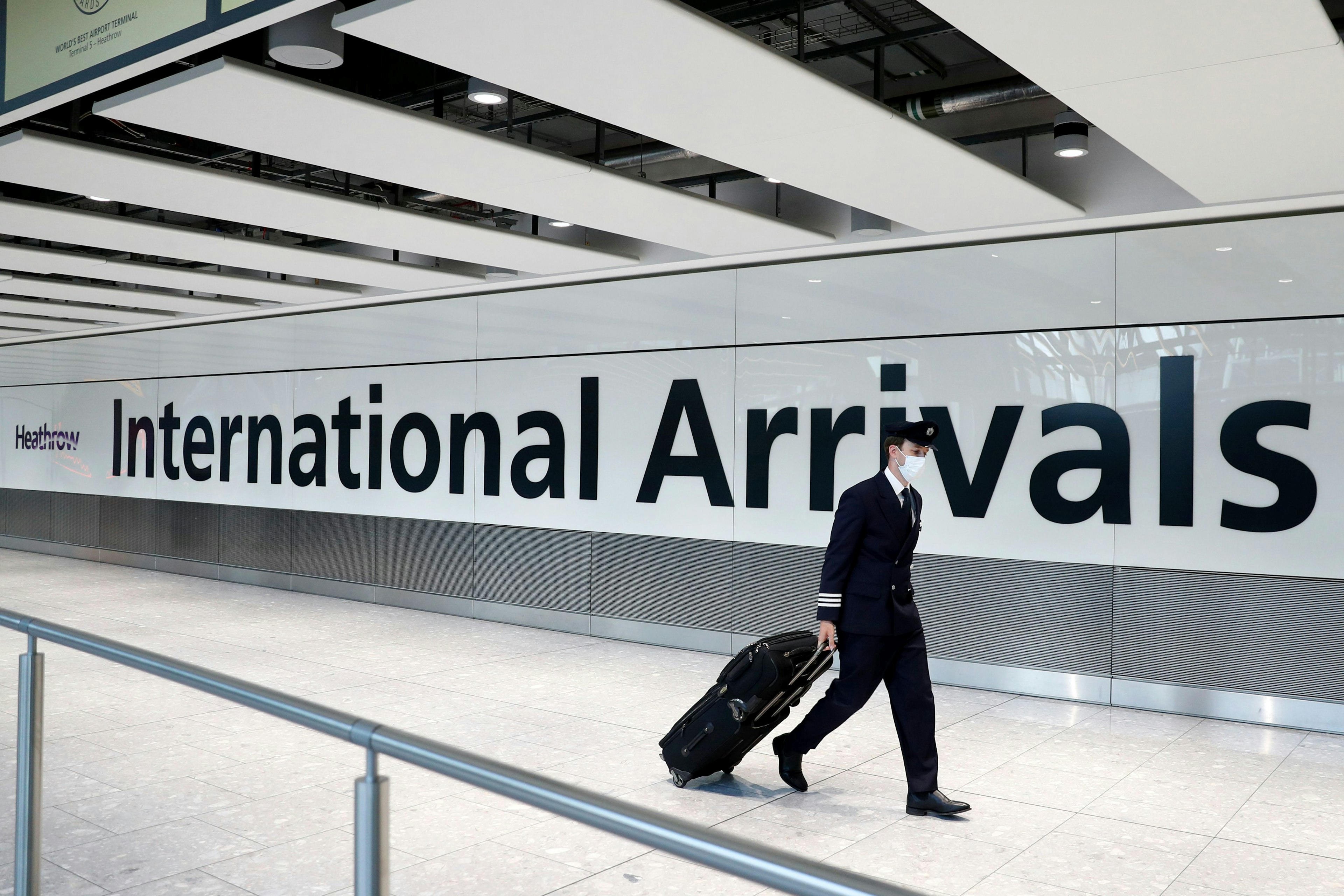 A pilot wears a facemask as he arrives at Terminal 5 at Heathrow airport