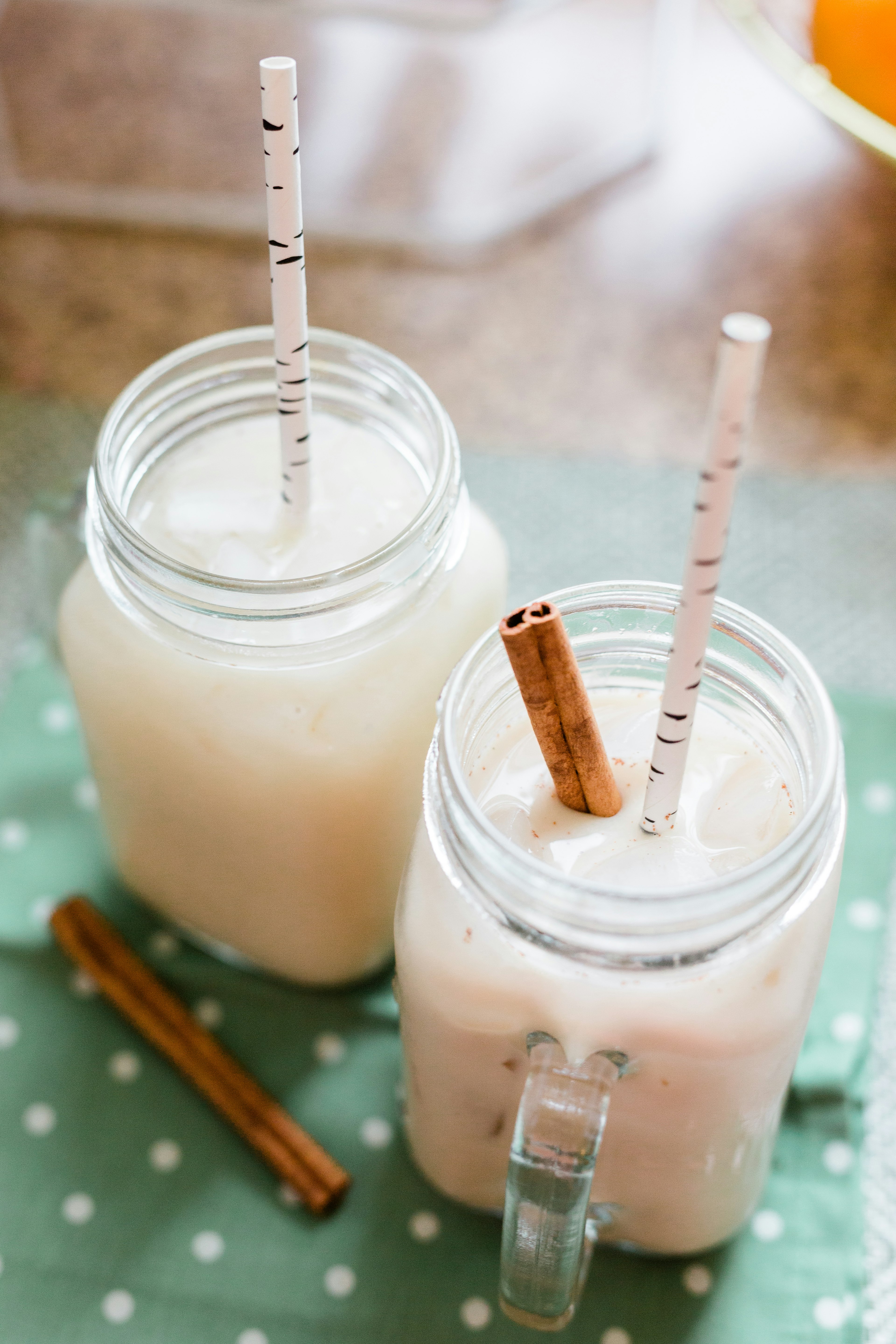 Refreshing Agua de horchata Drink in two glass mugs with a cinnamon stick and a straw on a green napkin