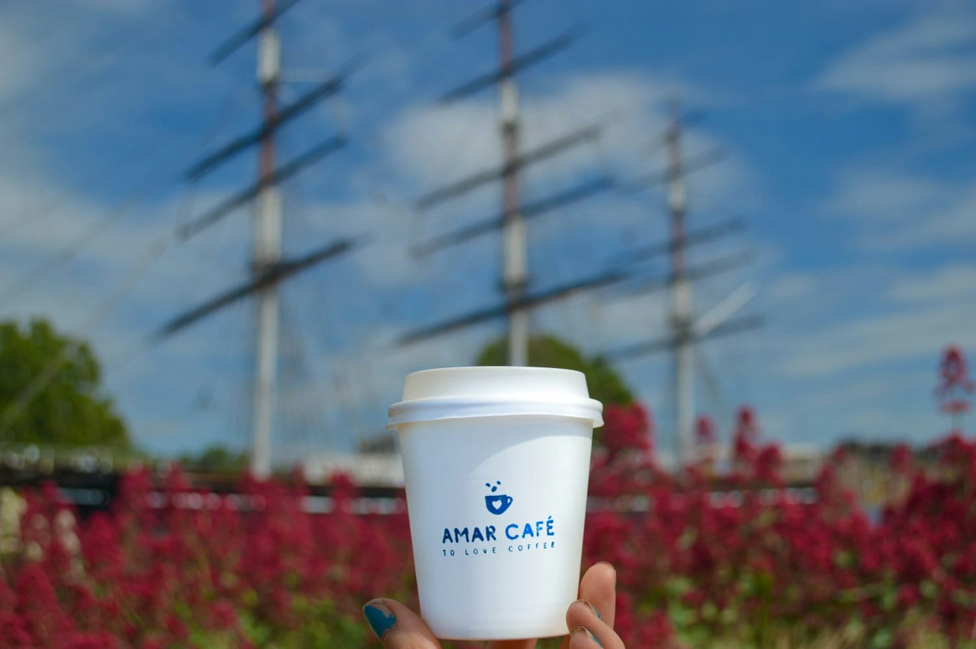 A takeaway coffee cup is held up against a blue sky backdrop