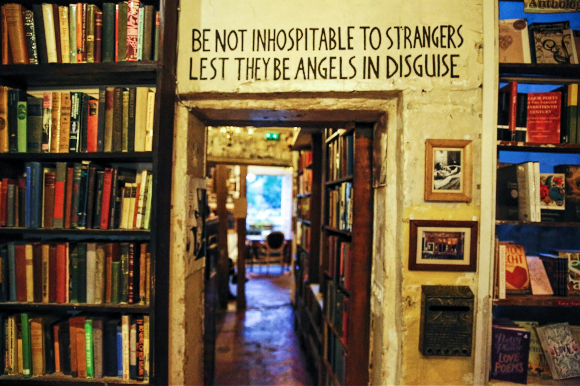 A motto reading "Be not inhospitable to strangers lest the be angels in disguise" painted above a doorway inside a bookshop