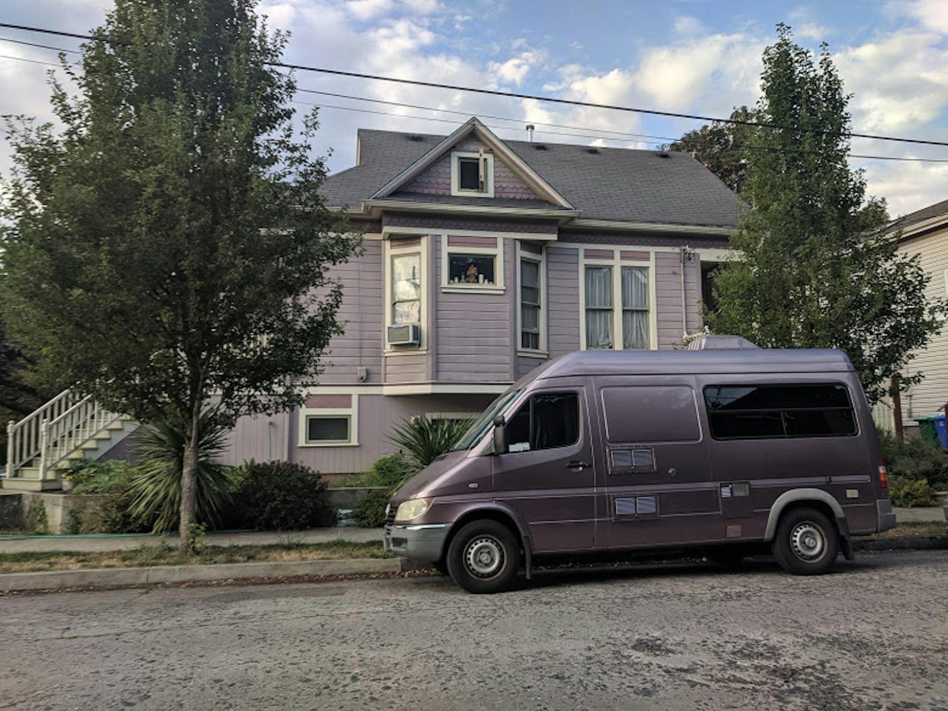 A custom lavender Sprinter van is parked in front of a matching Craftsman house in Portland, Oregon