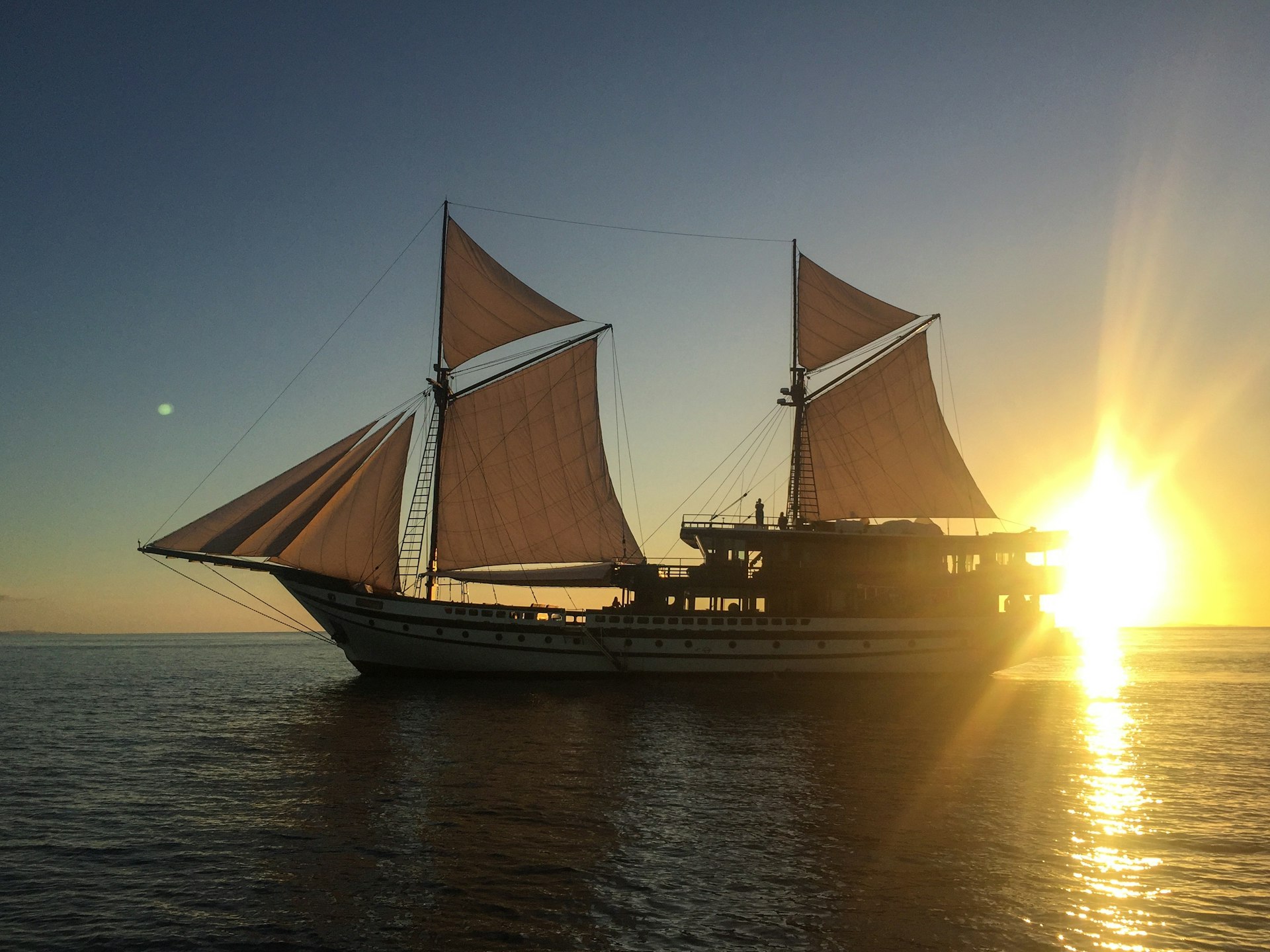 A phinisi yacht with the sun in the background