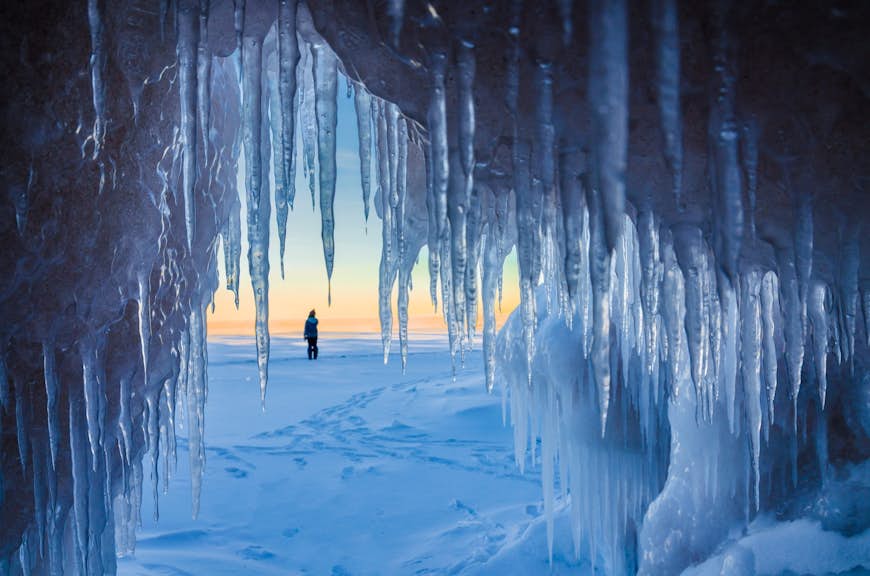 A shot looking outwards from the mouth of a cave to a snowy landscape. The cave is covered in icicles