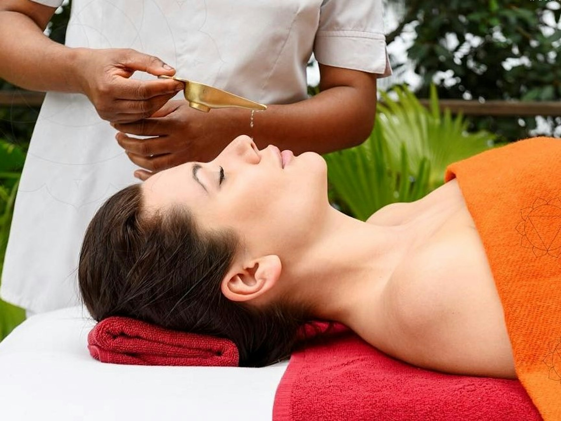 A woman undergoes a chakra cleansing at the Andana in the Himalayas spa. The customer lies on her back while a staff member pours oil into her nose.