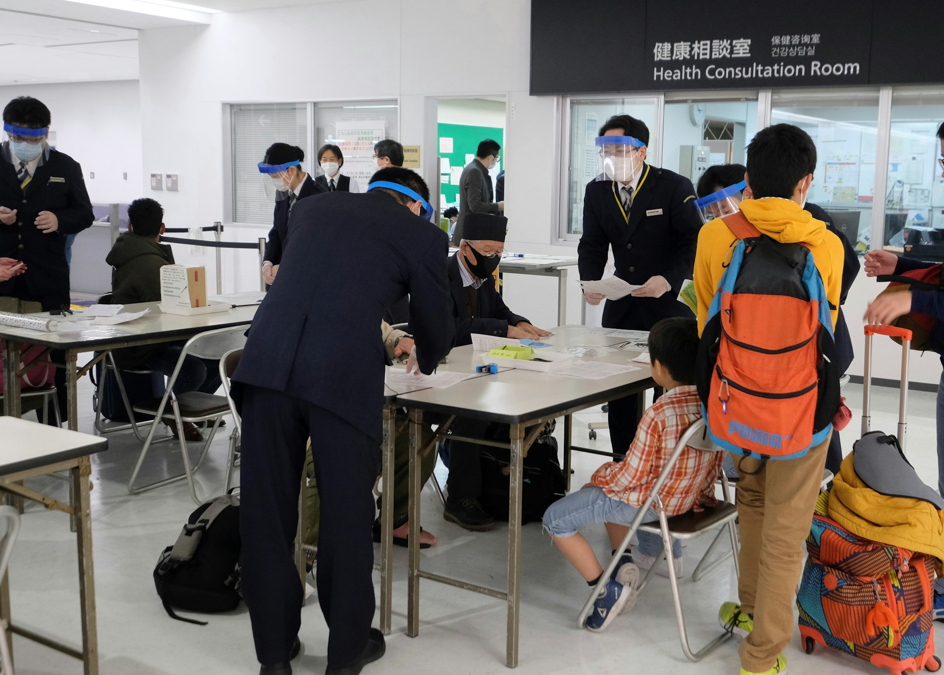 Officers wearing face masks and shields assist passengers arriving from Hong Kong, to fill out quarantine forms at Narita airport, Chiba prefecture