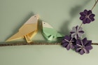 To paper origami birds perched on a tree branch with purple cosmos origami flowers on. Space for copy.