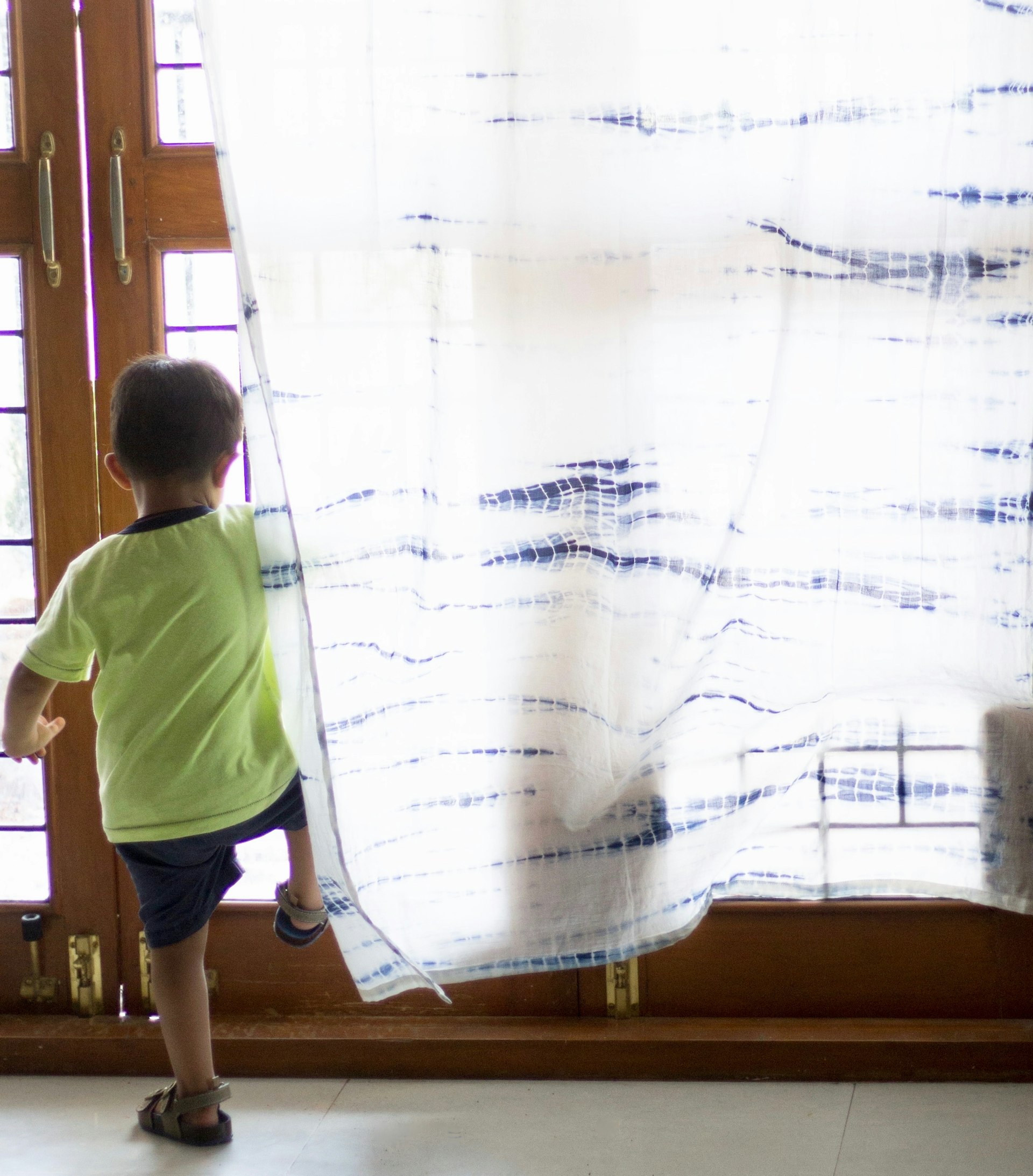 A kid in a green shirt in front Kari by Kriti's shibori curtains