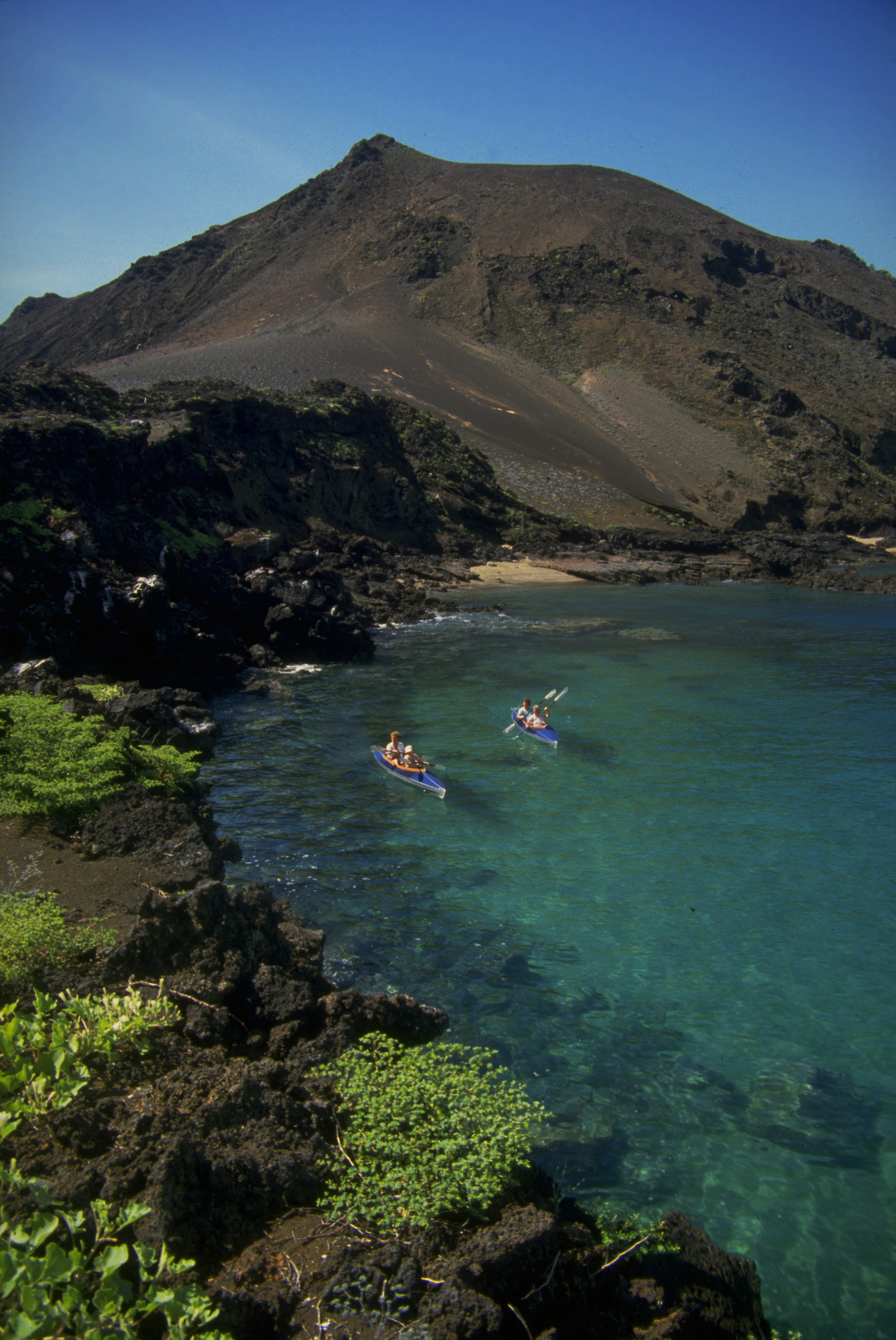 Two kayaks, each with two kayakers, in a wide curving bay backed by a dark rocky coastline