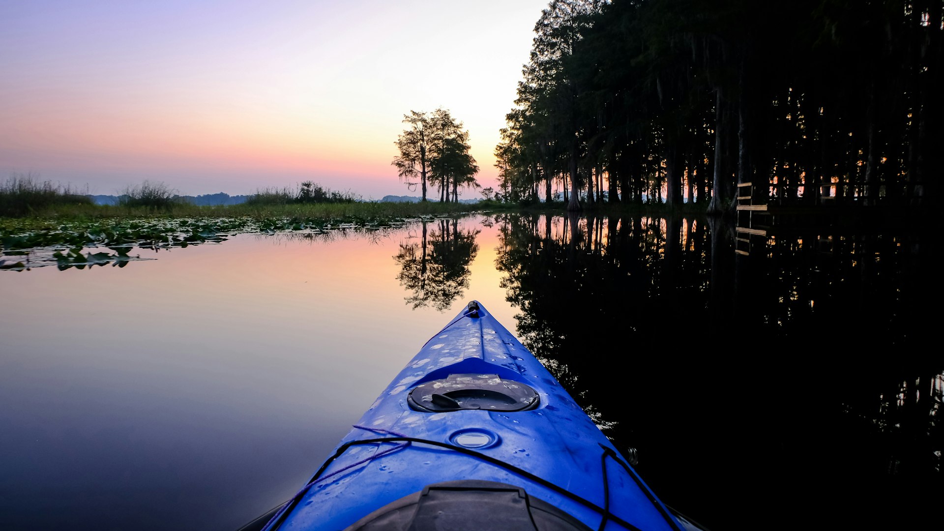 A photo taken from the front of a kayak of a peaceful lake at dusk