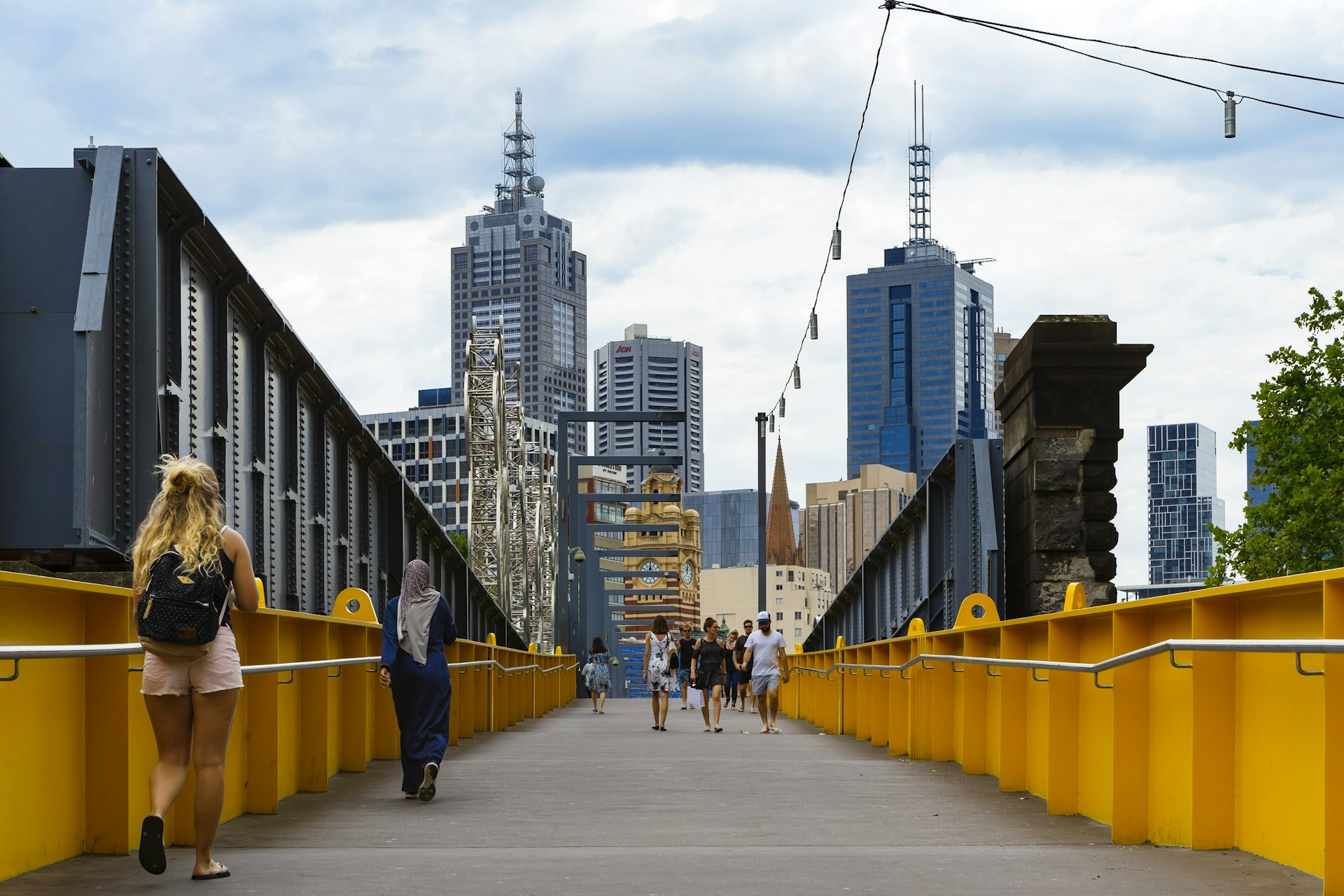 People walking across a bridge with a city skyline in the background