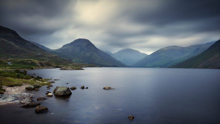 A moody shot of a mountain peak rising above a lake with low gray clouds in the sky