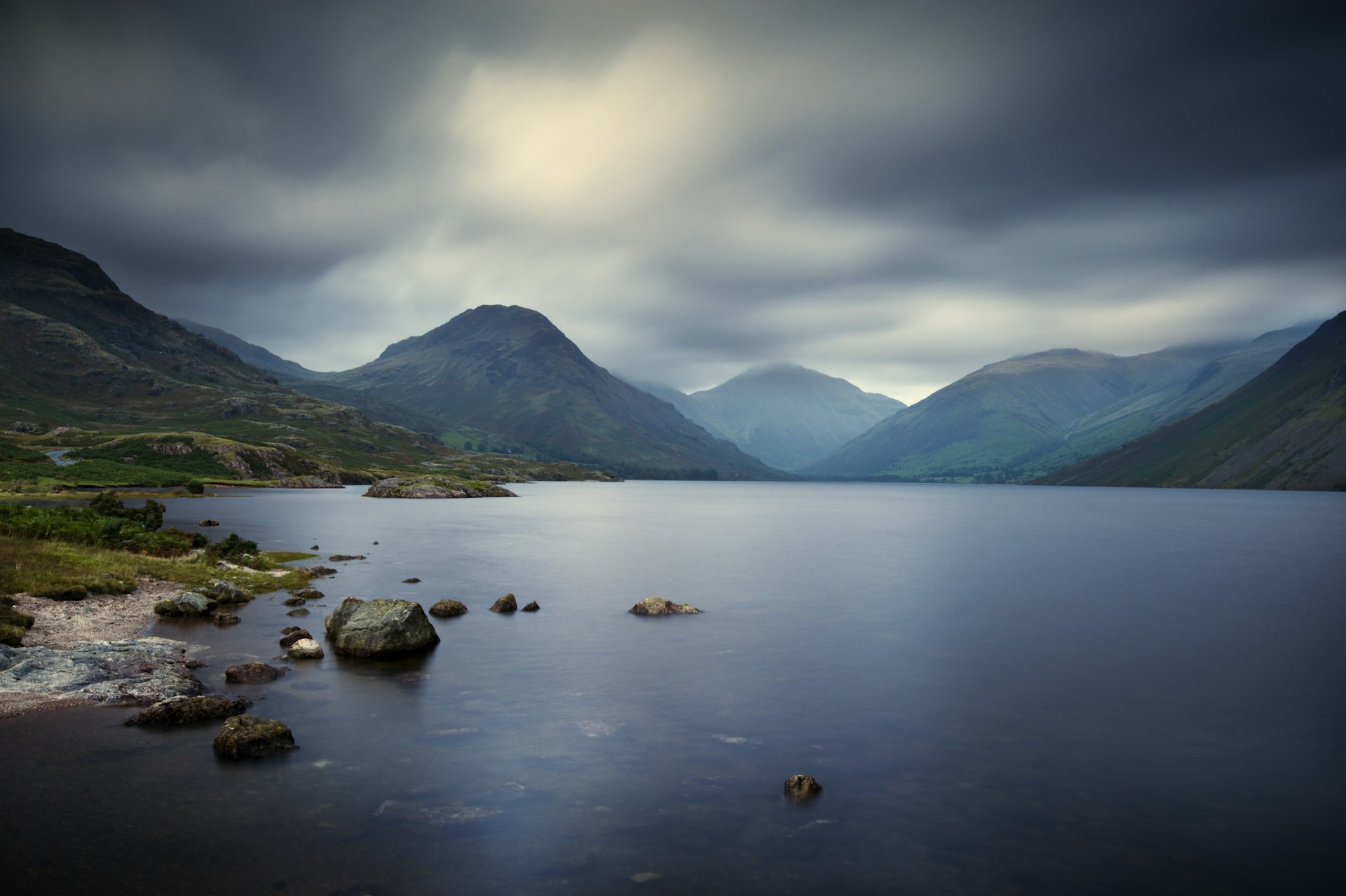 A shot a vast empty lake surrounded by peaks. The light is quite grey and moody