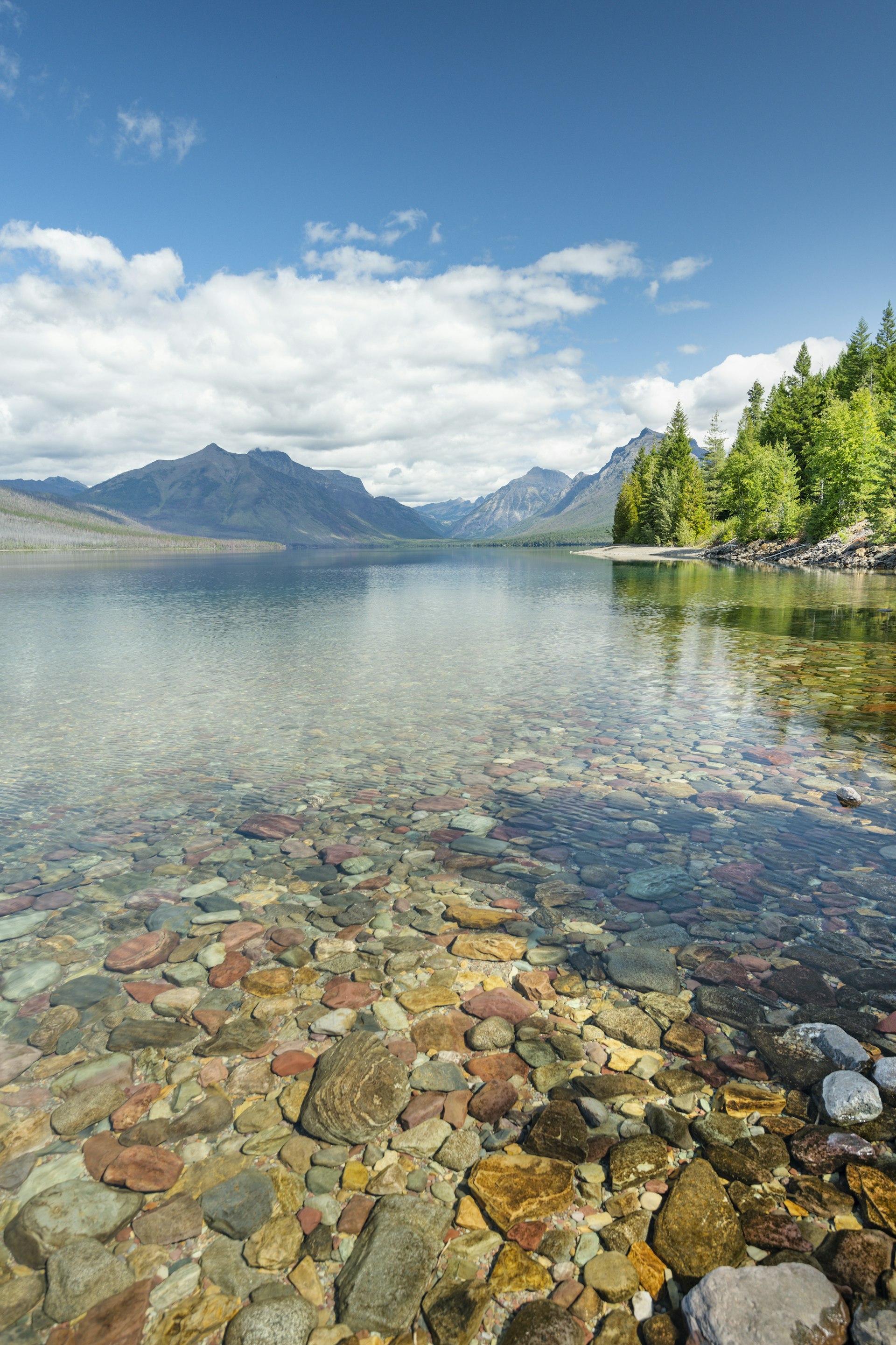 A lake, with shallow water so clear that colorful pebbles at the bottom of the lake are evident. 