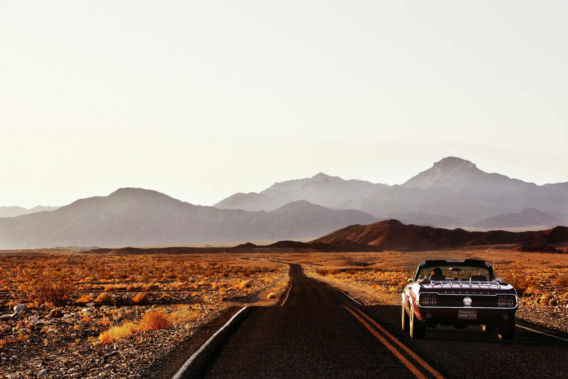 A car driving down a road that cuts through a desert landscape