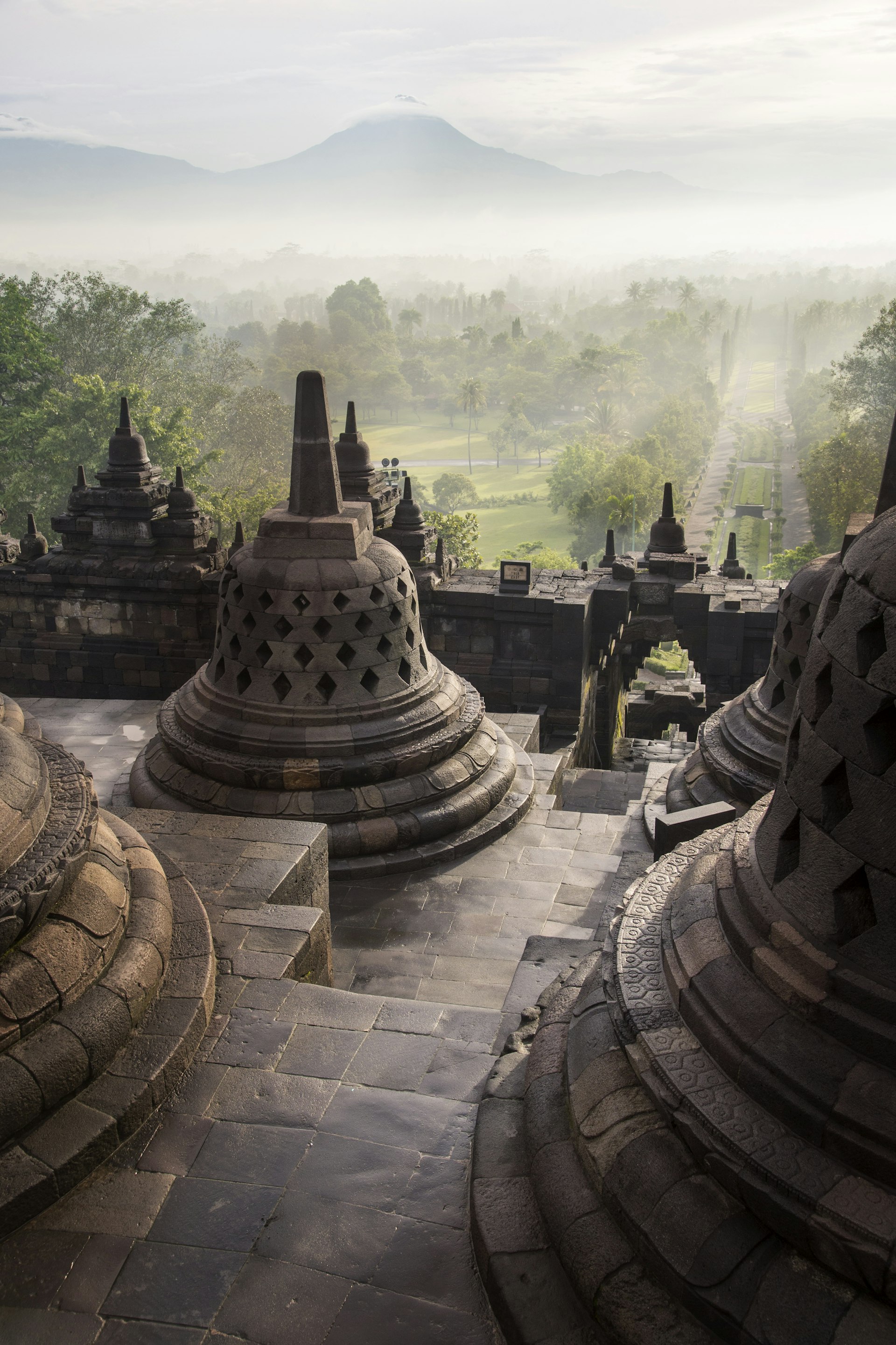 Stupas at the top of Borobudur, with the volcanic peak of Merapi above the morning mist in the background.