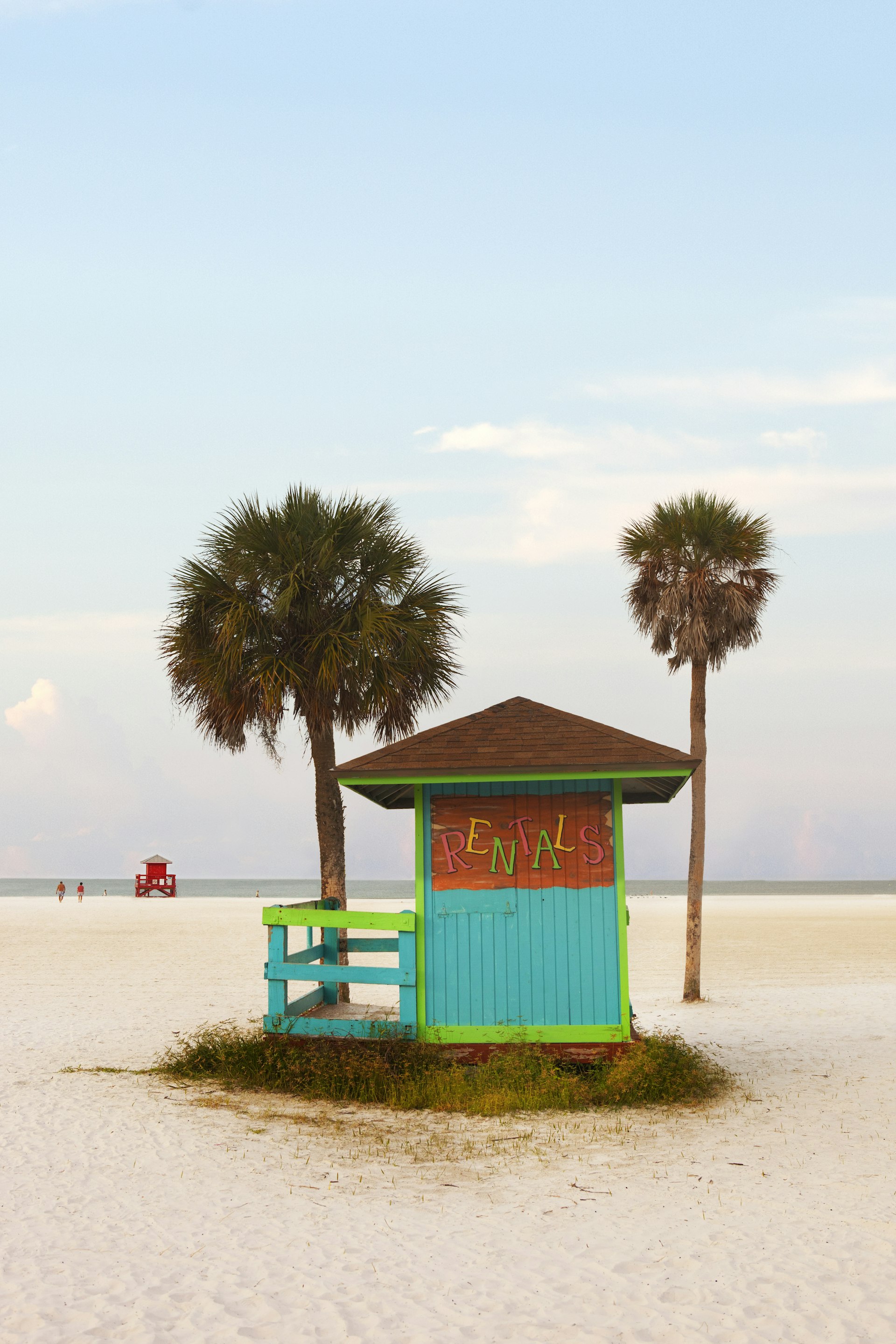 A colorful wooden rental hut sits between two palm trees on Siesta Key beach.