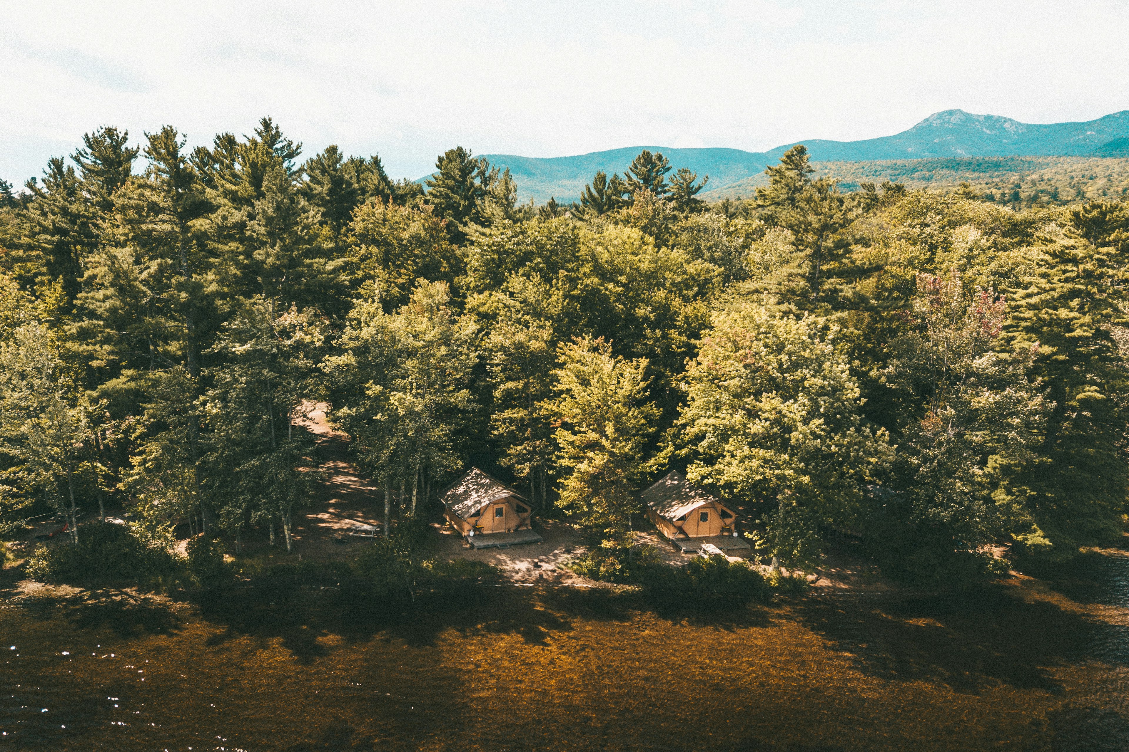 Aerial shot of thick woodland with two wooden cabins poking out by the side of a lake