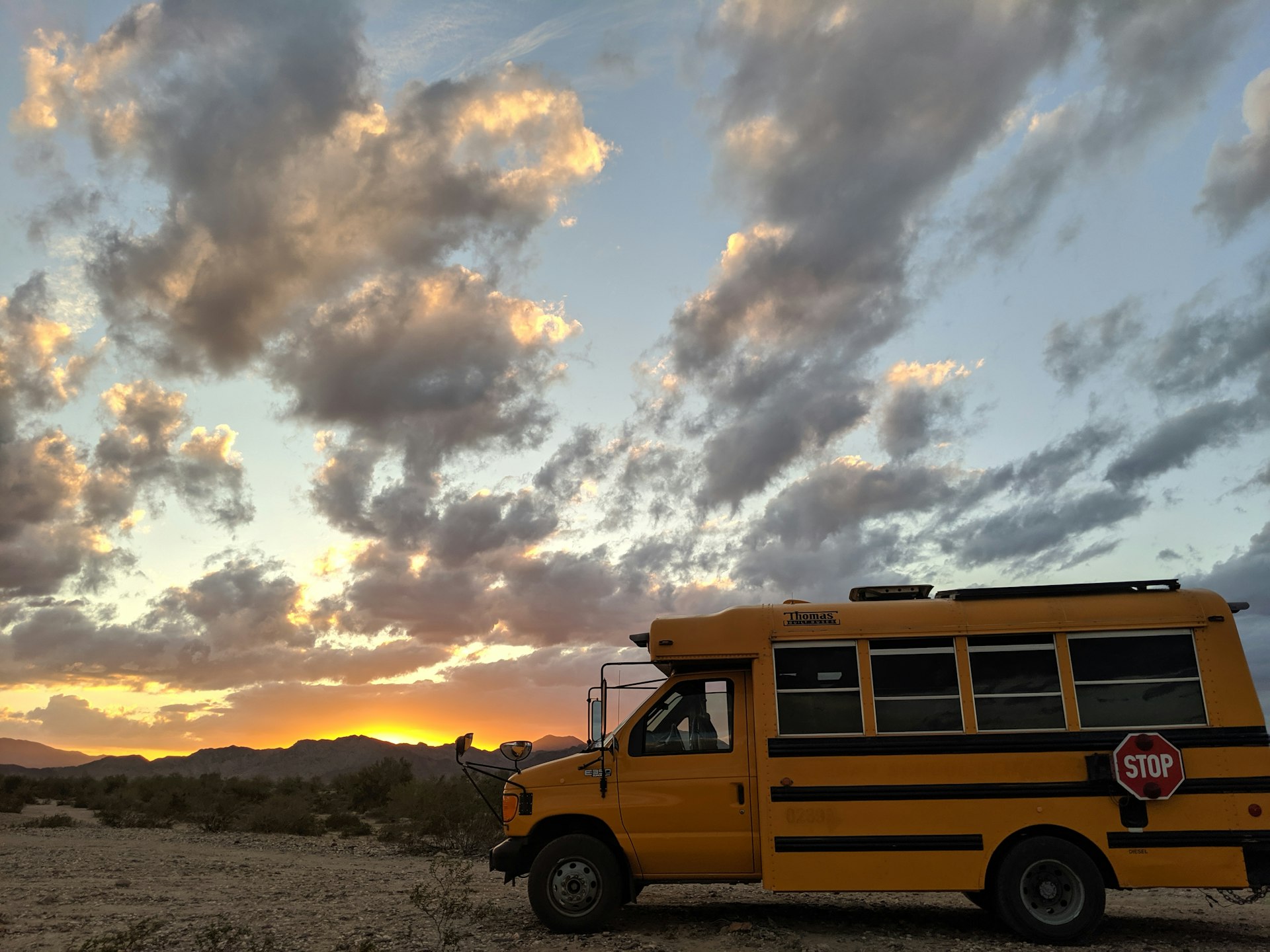 A short yellow school bus against a brilliant desert sunset