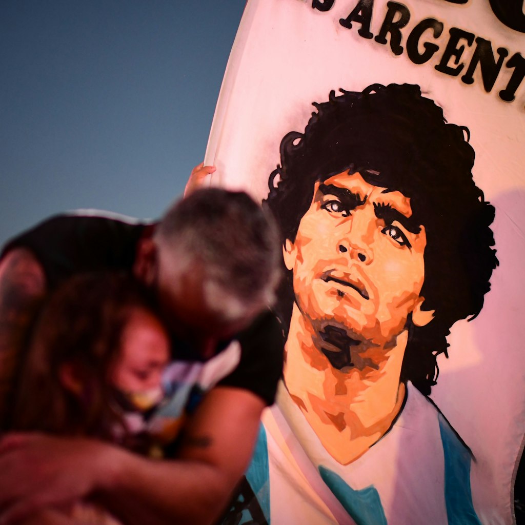 TOPSHOT - A father and her daughter, fans of Argentinian football legend Diego Maradona, mourn as they gather by the Obelisk to pay homage on the day of his death in Buenos Aires, on November 25, 2020. - The body of Argentine football legend Diego Maradona, who died earlier today, will lie in state at the presidential palace in Buenos Aires during three days of national mourning, the presidency announced. (Photo by RONALDO SCHEMIDT / AFP) (Photo by RONALDO SCHEMIDT/AFP via Getty Images)