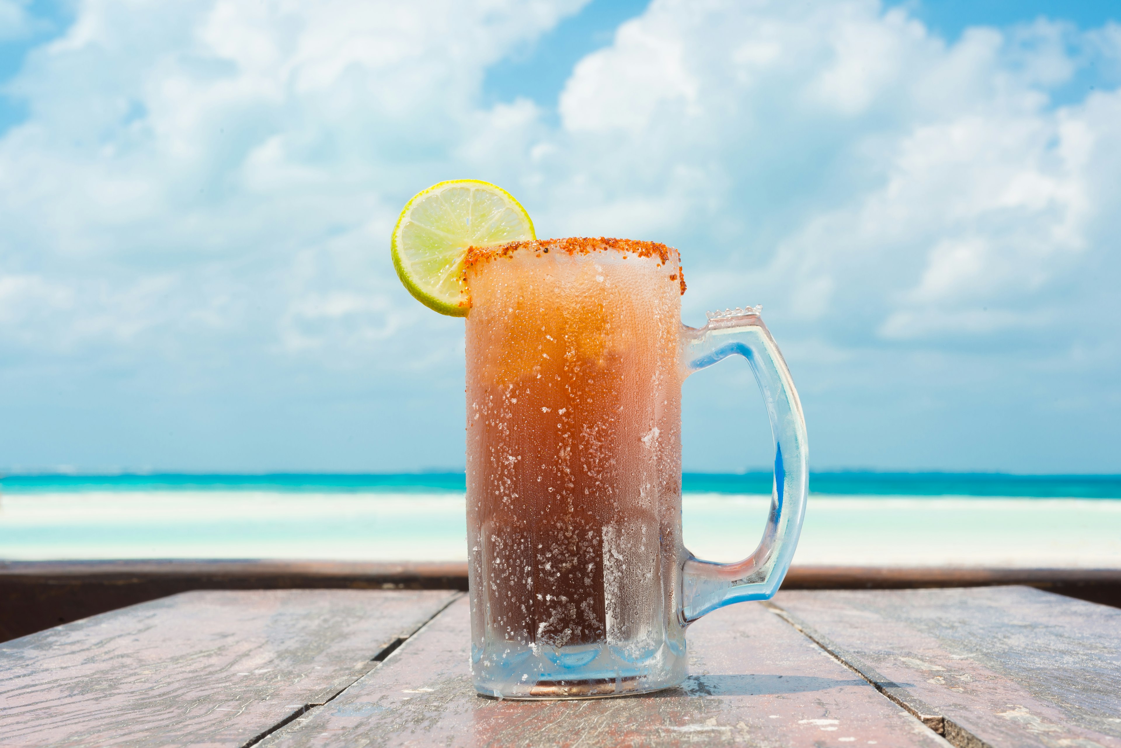 "Michelada" beer jar with a lemon slice on a blue sky with clouds