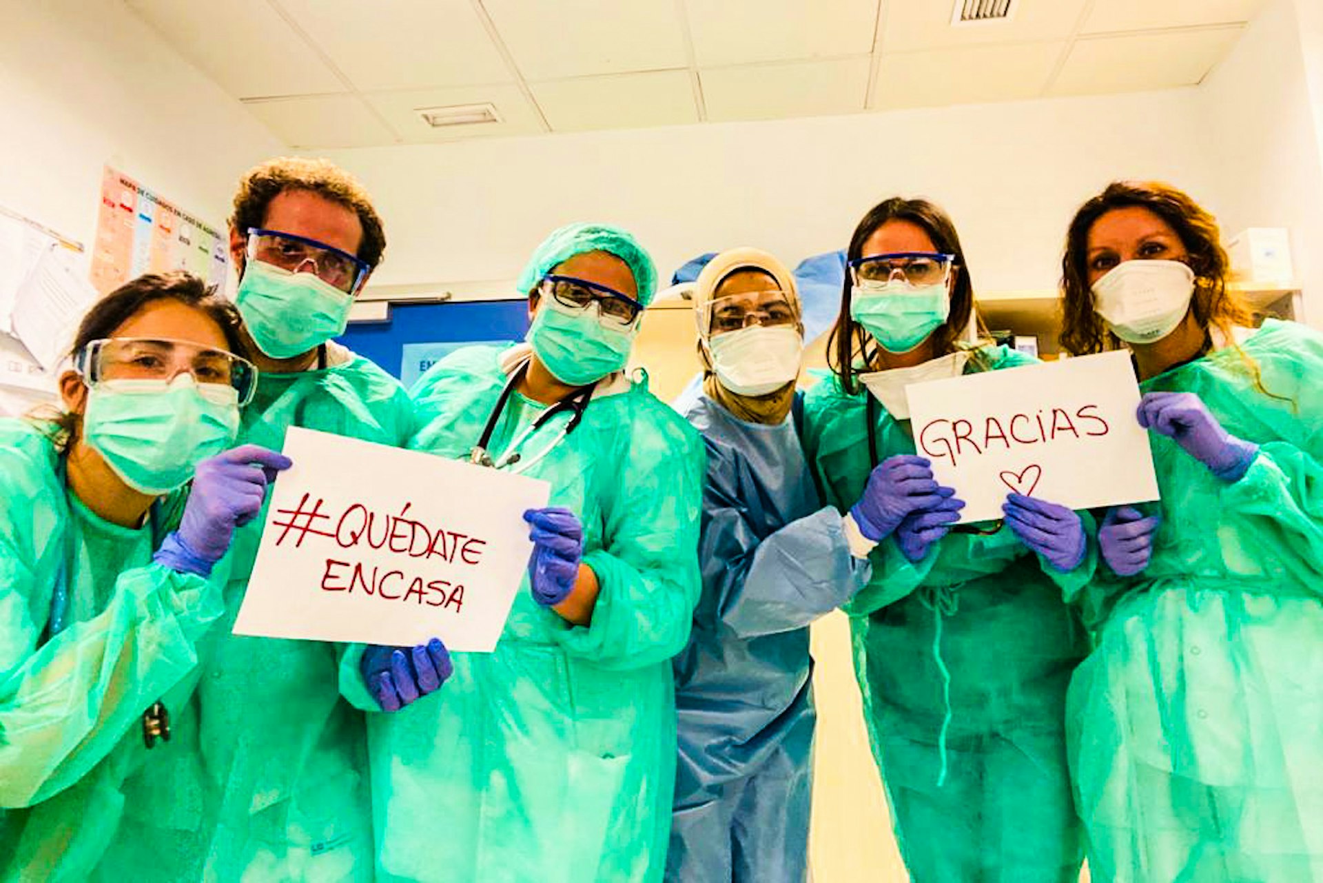 A group of doctors in protective gear hold up a sign saying 'Gracias', meaning Thank You in Spanish