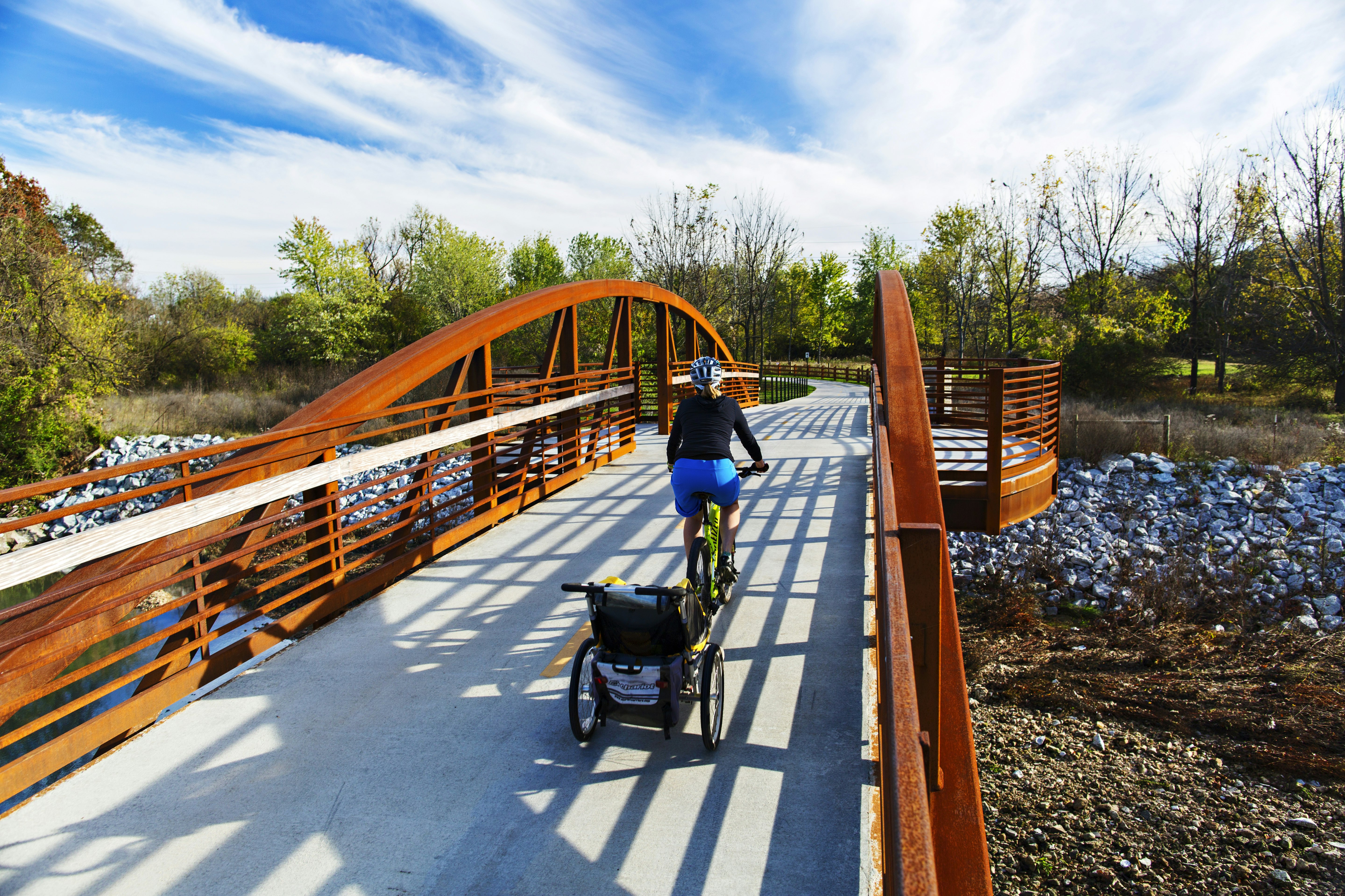 Woman rides bike pulling child carrier on trail