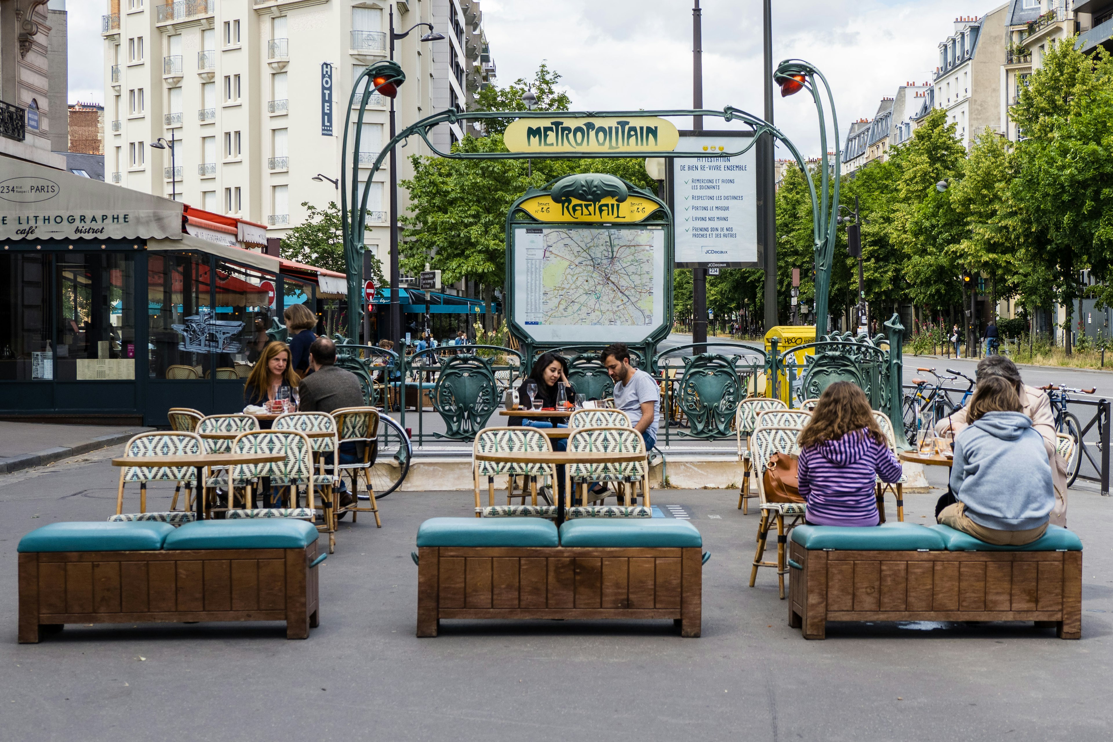 People sit at a terrace in front of the Raspail metro station in the 14th quarter of Paris,