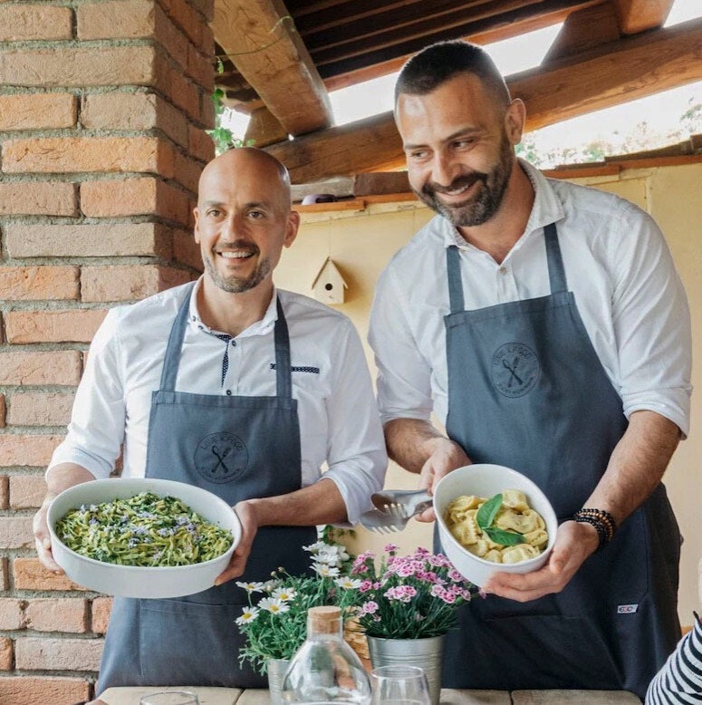 Two chefs holding pasta dishes