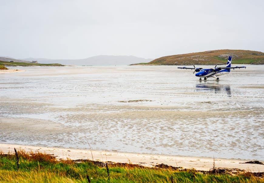 A small airplane sits on the flat sands of a beach with the sea in the distance
