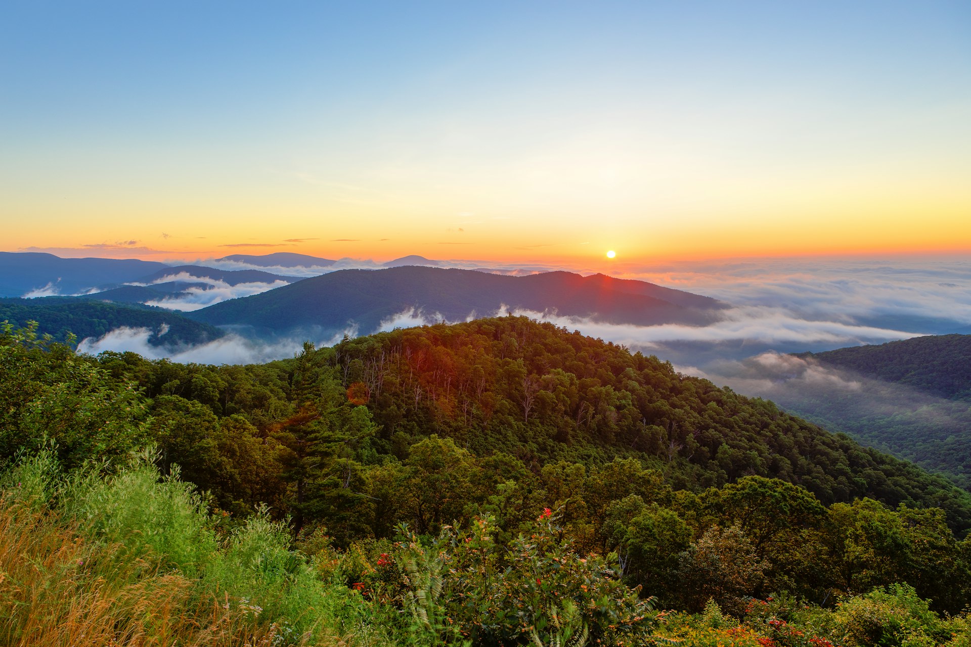The sun rises over vast hilly landscape, with some cloud covering the valleys below