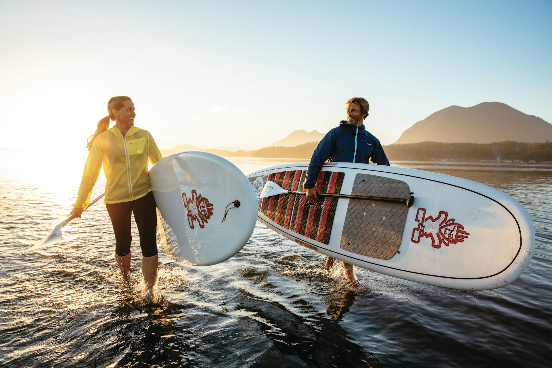 Two paddleboarders head in from the surf carrying their boards and oars