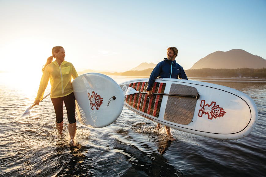 Two paddleboarders head in from the surf carrying their boards and oars