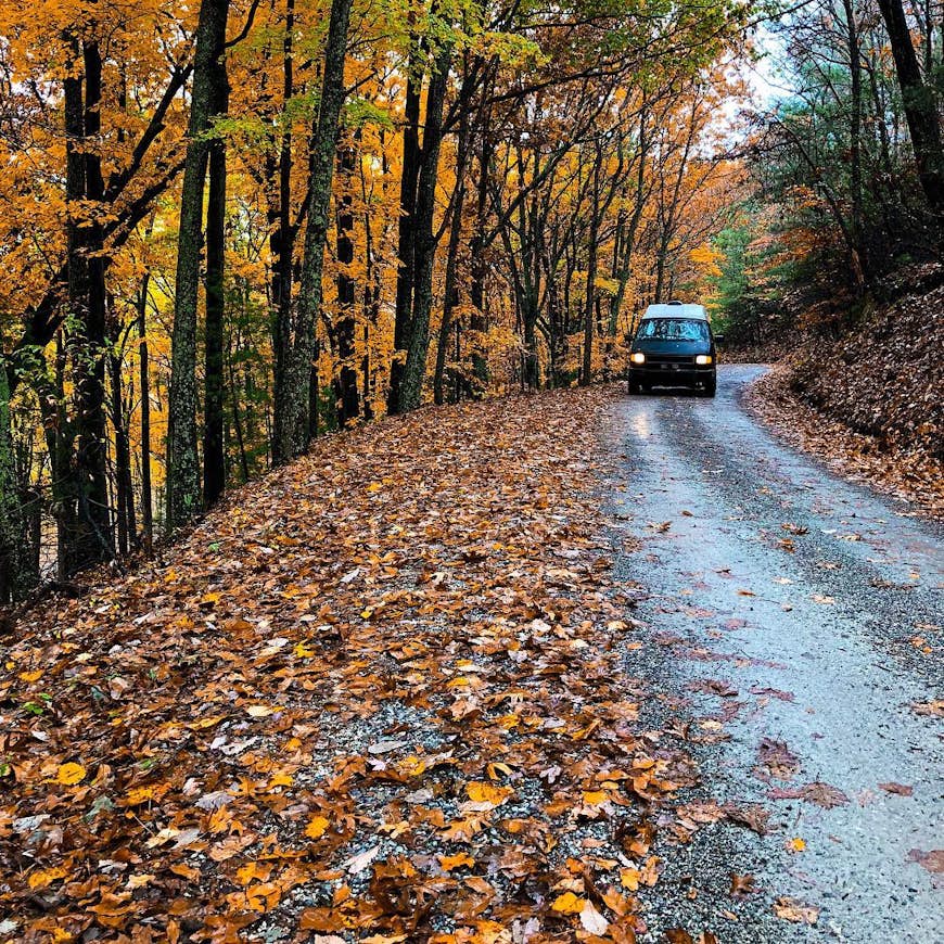 A camper van drives on a road surrounded by red, orange and yellow fall colors in Tennessee